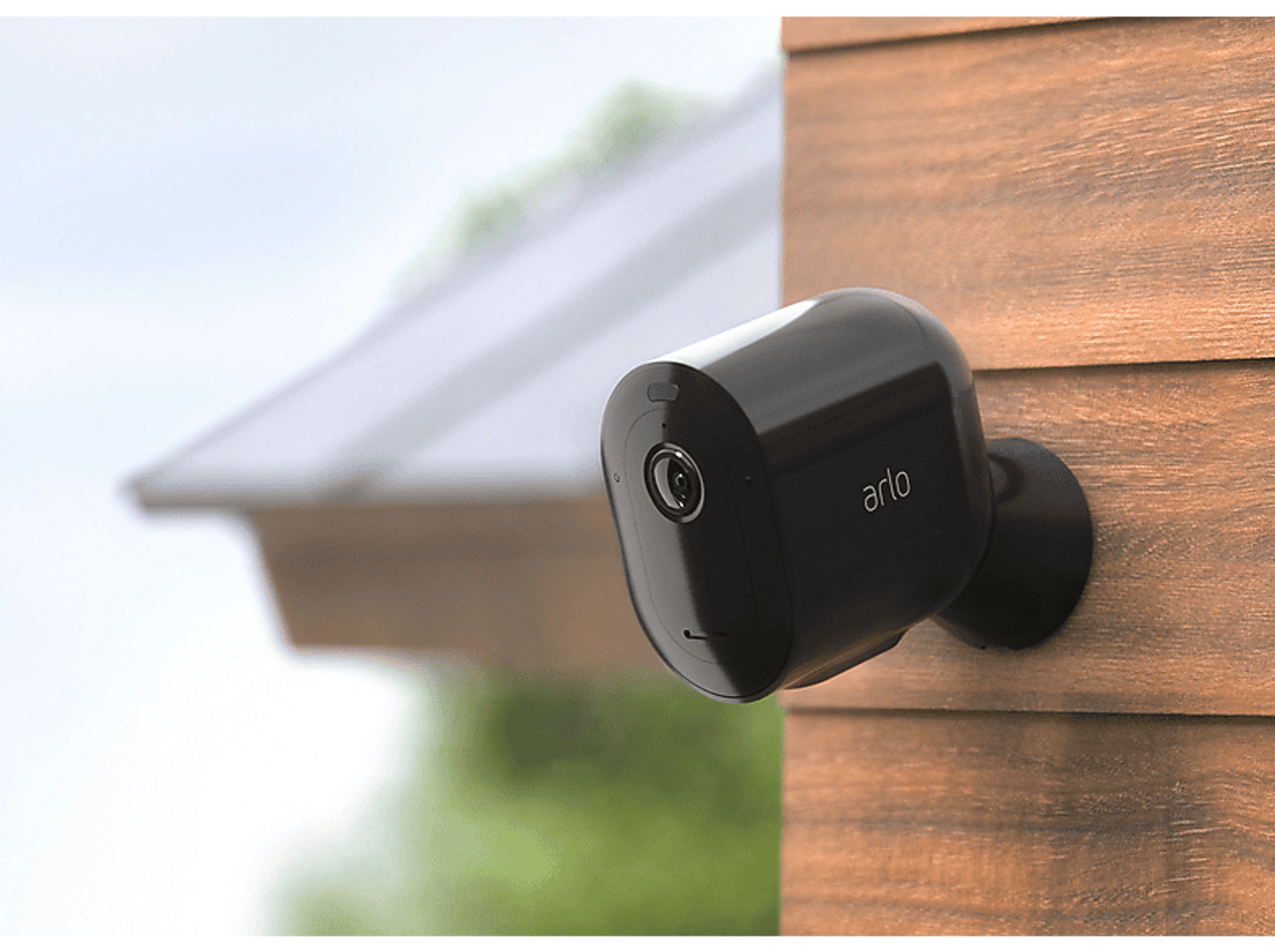 Czarna kamera bezpieczeństwa Arlo na drewnie. Biały dach w tle.