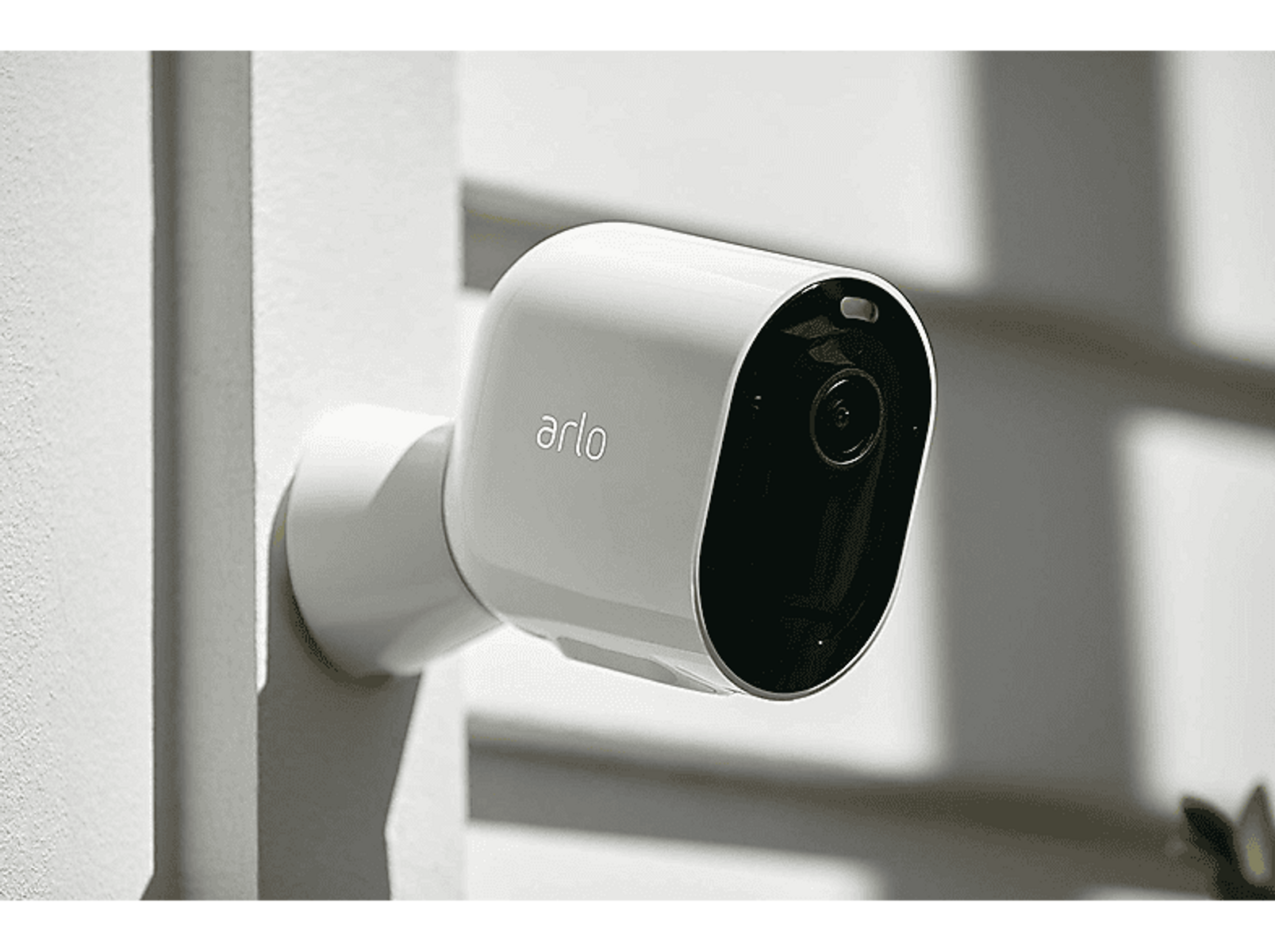 Biała kamera bezpieczeństwa zamontowana na białej ścianie, z marką 'arlo'.