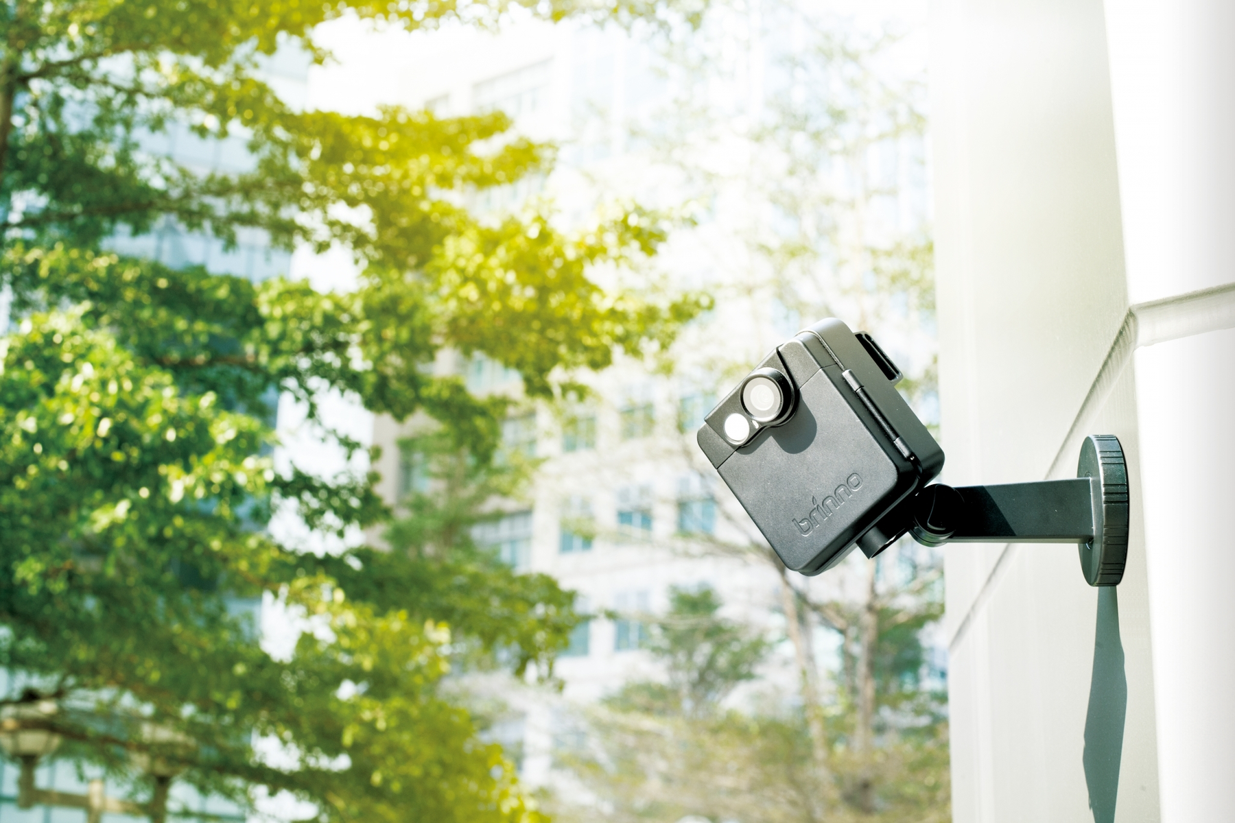 Telecamera di sicurezza per esterni montata su un muro. Alberi verdi e un edificio sullo sfondo.