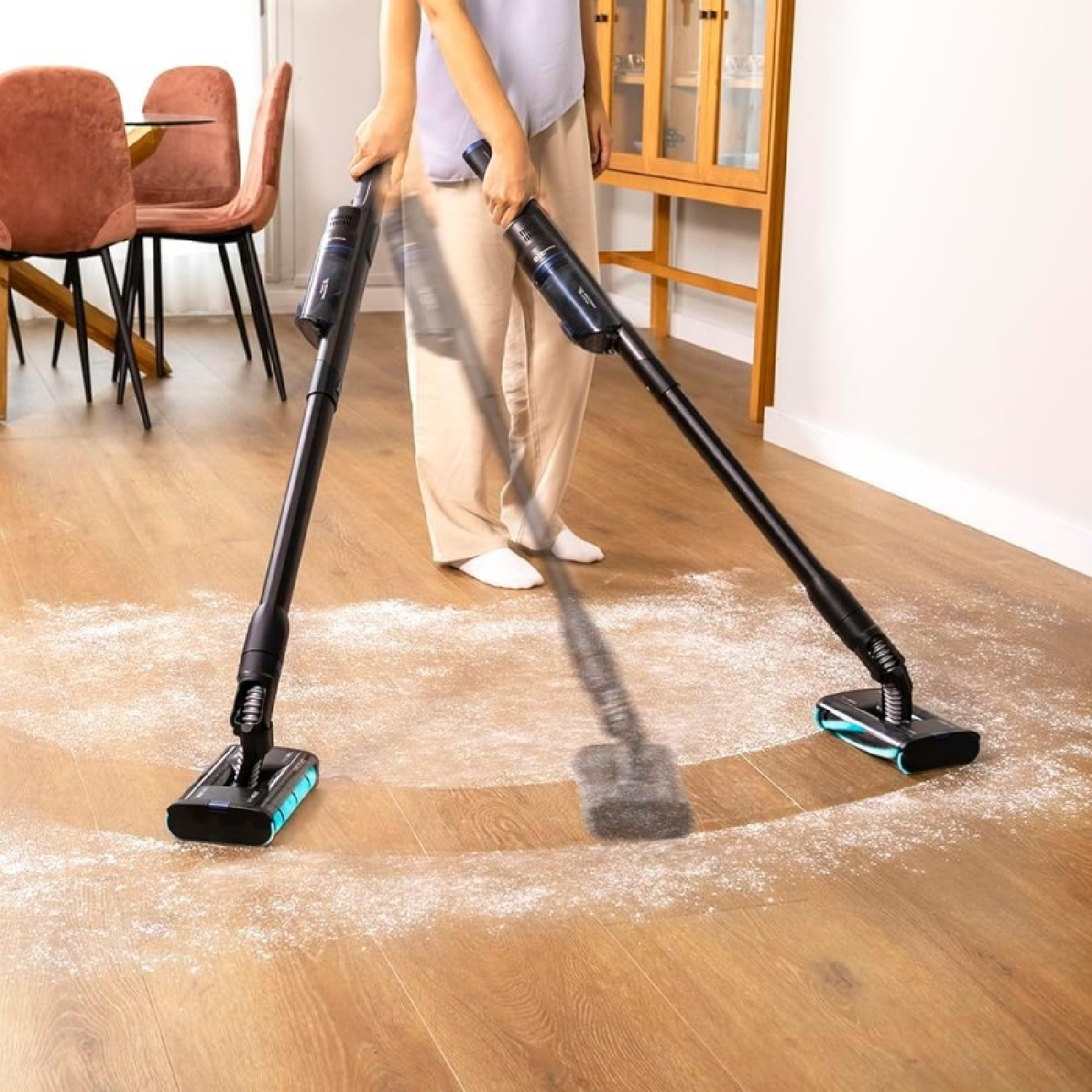 Una donna usa un aspirapolvere su un pavimento in legno, pulendo della polvere bianca.