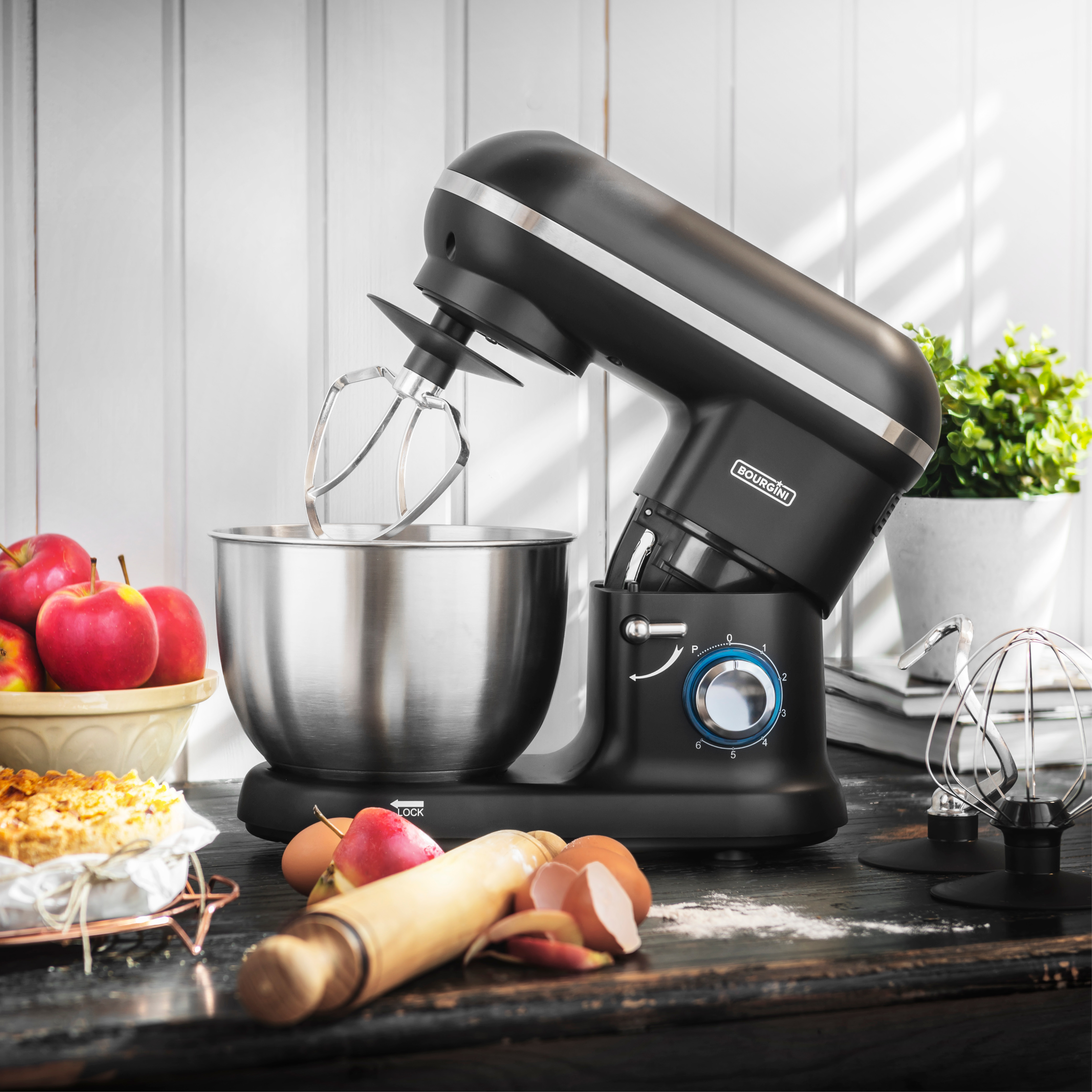 Ein schwarzer Küchenmixer mit Aufsätzen. Äpfel und Eier liegen auf der Theke.