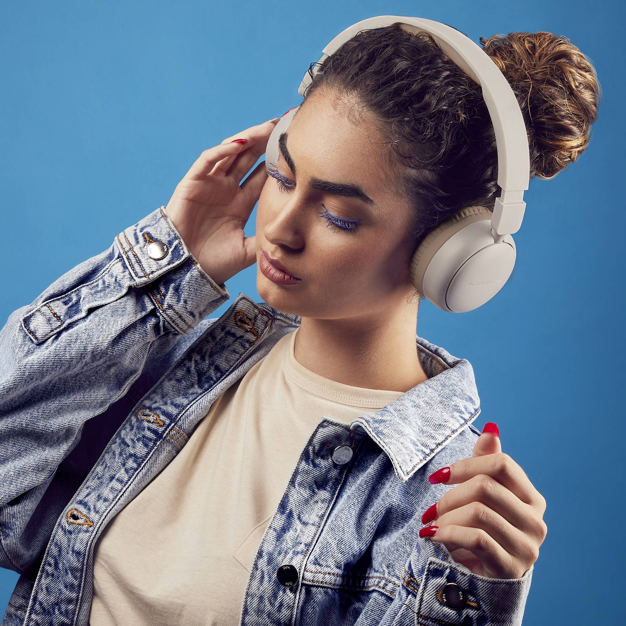 Kobieta w słuchawkach i dżinsowej kurtce, niebieskie tło.
