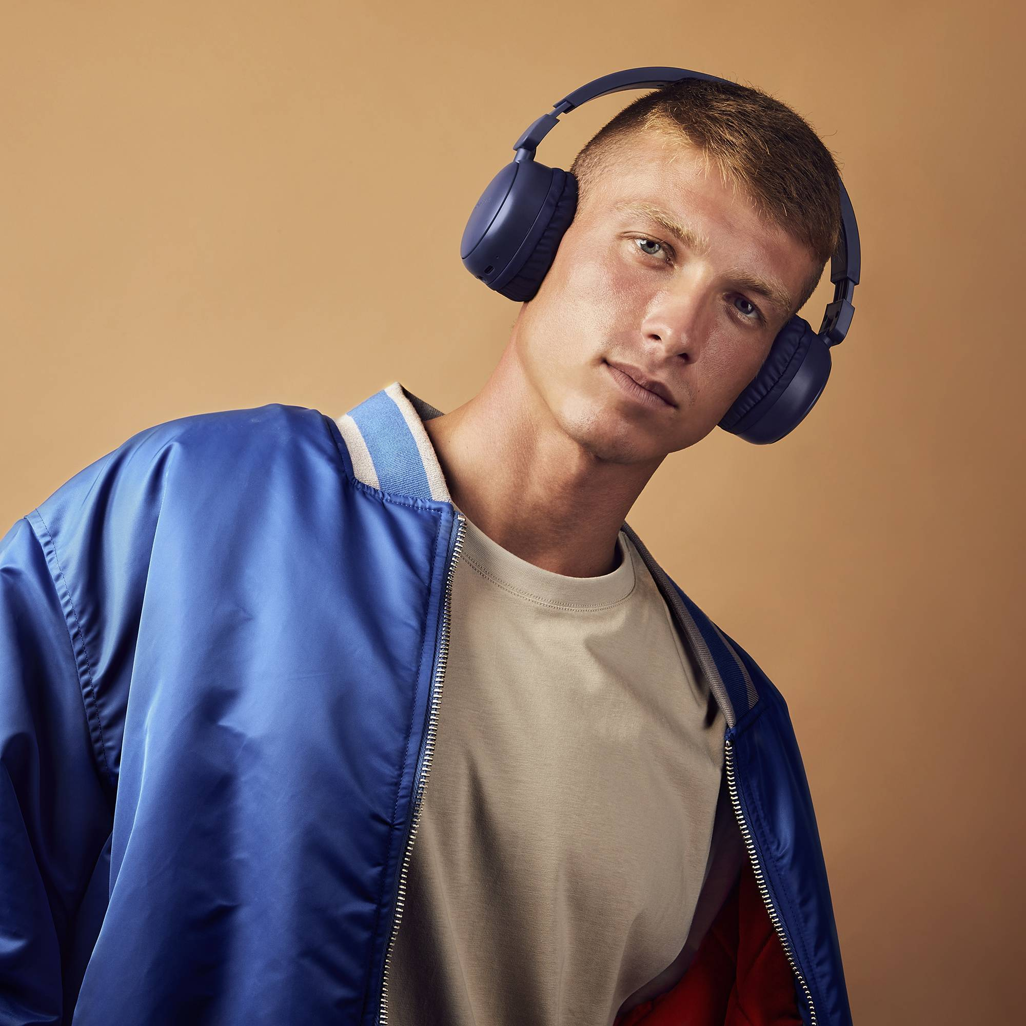 Ein junger Mann in einer blauen Jacke und Kopfhörern, der in die Kamera schaut.