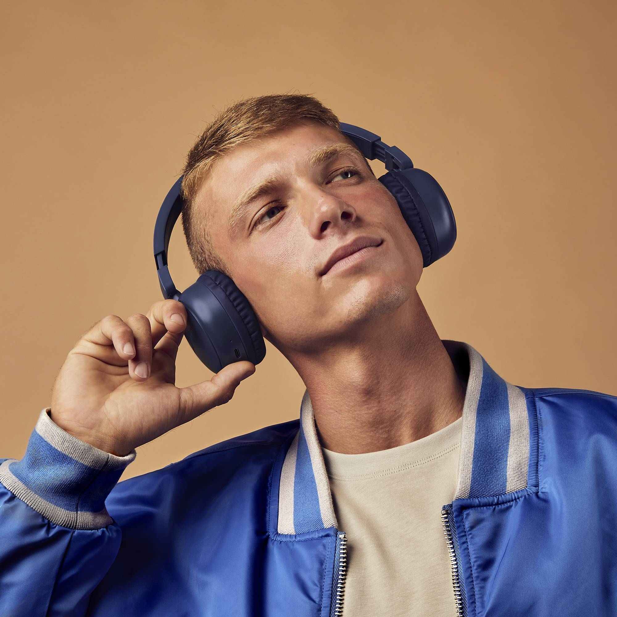 Ein junger Mann mit blauen Kopfhörern und einer blauen Jacke, der nach oben schaut.