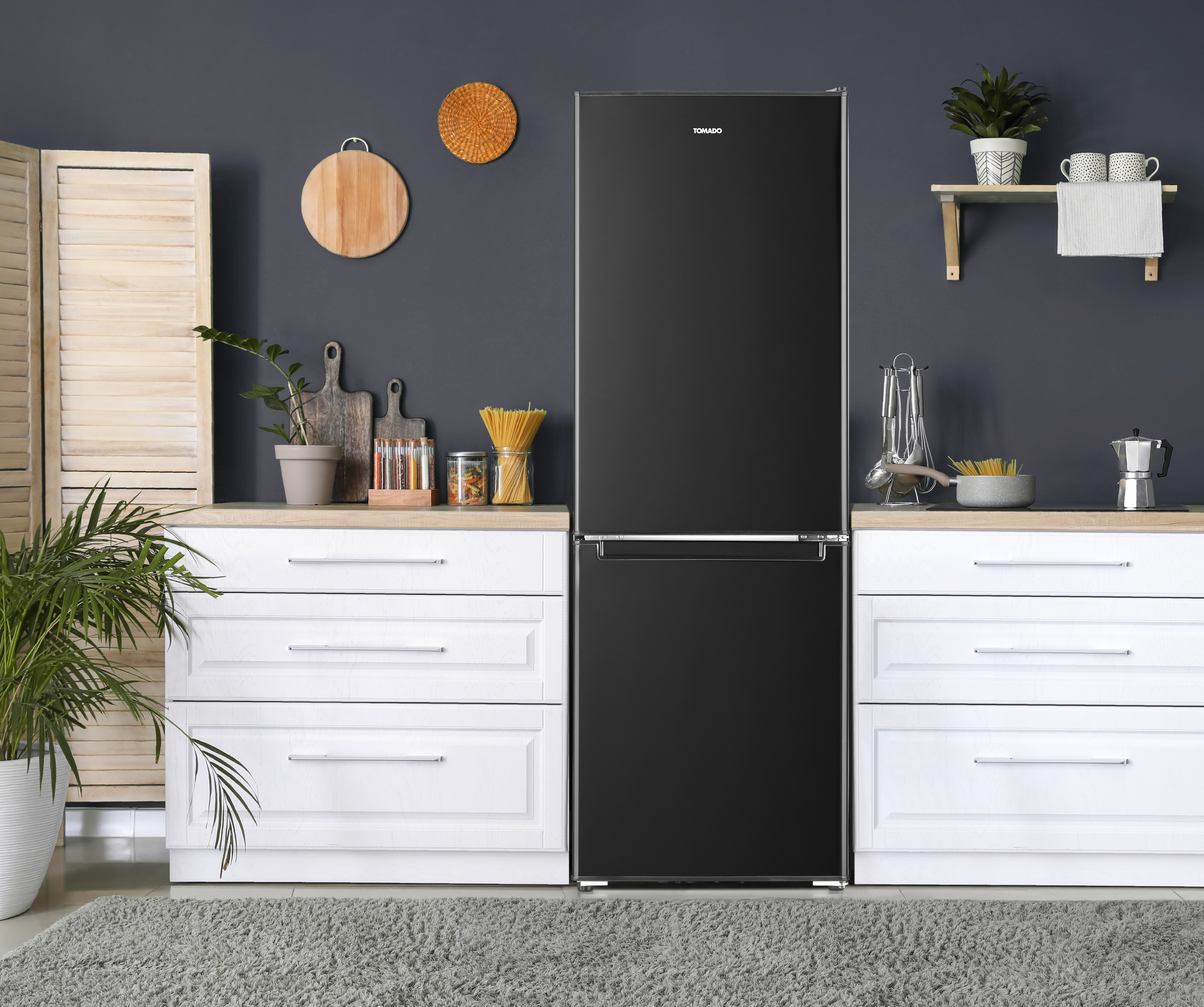 Black refrigerator in a kitchen. White cabinets, wooden cutting boards, and plants are visible.