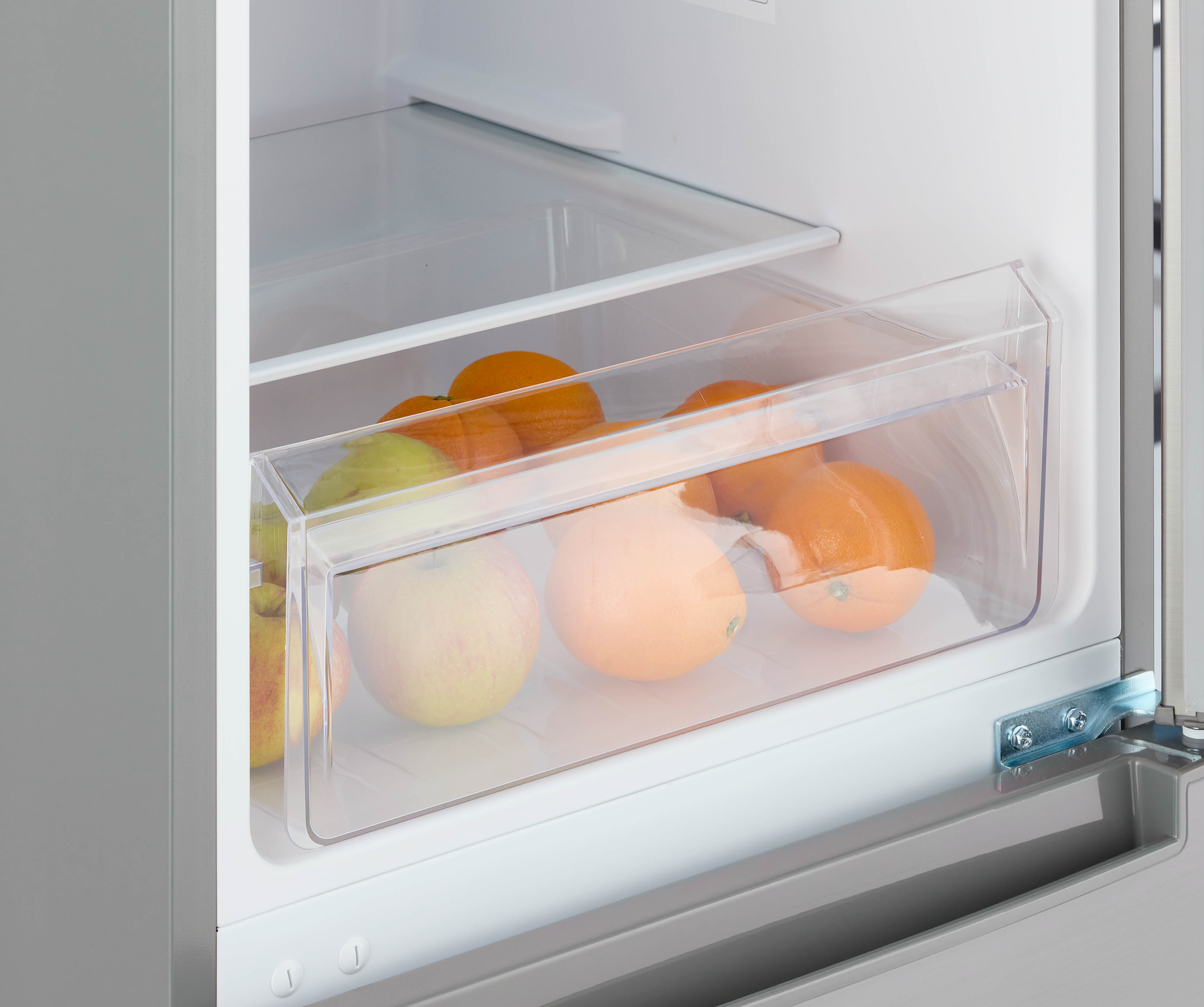 A transparent drawer in a fridge filled with oranges, apples and a green pear. Grey background.