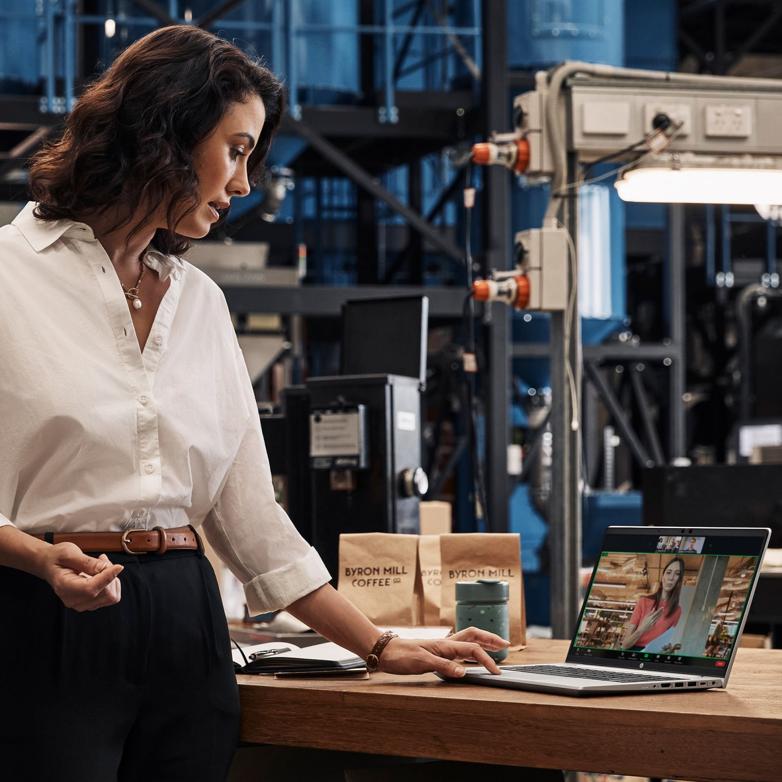 Kobieta w białej koszuli patrzy na laptopa podczas rozmowy wideo w fabryce.