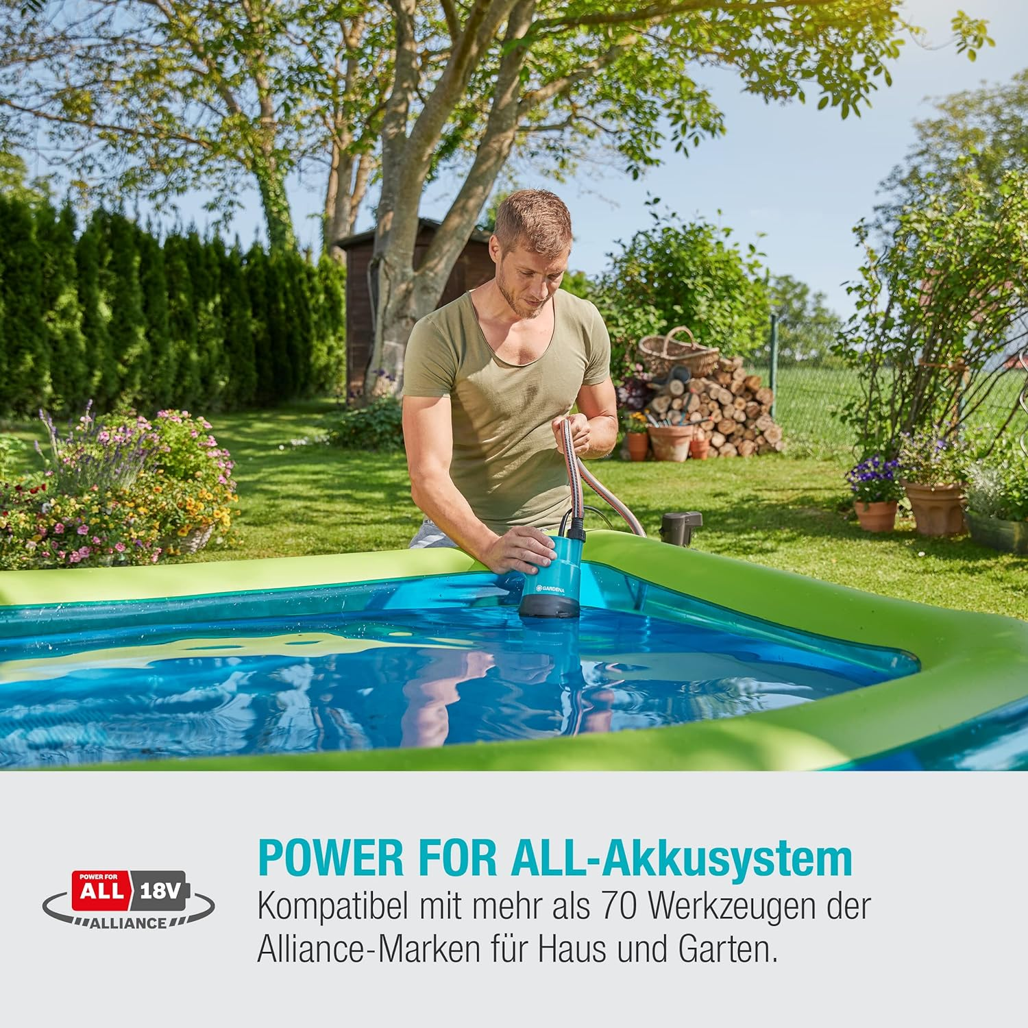 Un homme utilise une pompe dans une piscine bleue, avec des bords verts. Arrière-plan : plantes et cabane.