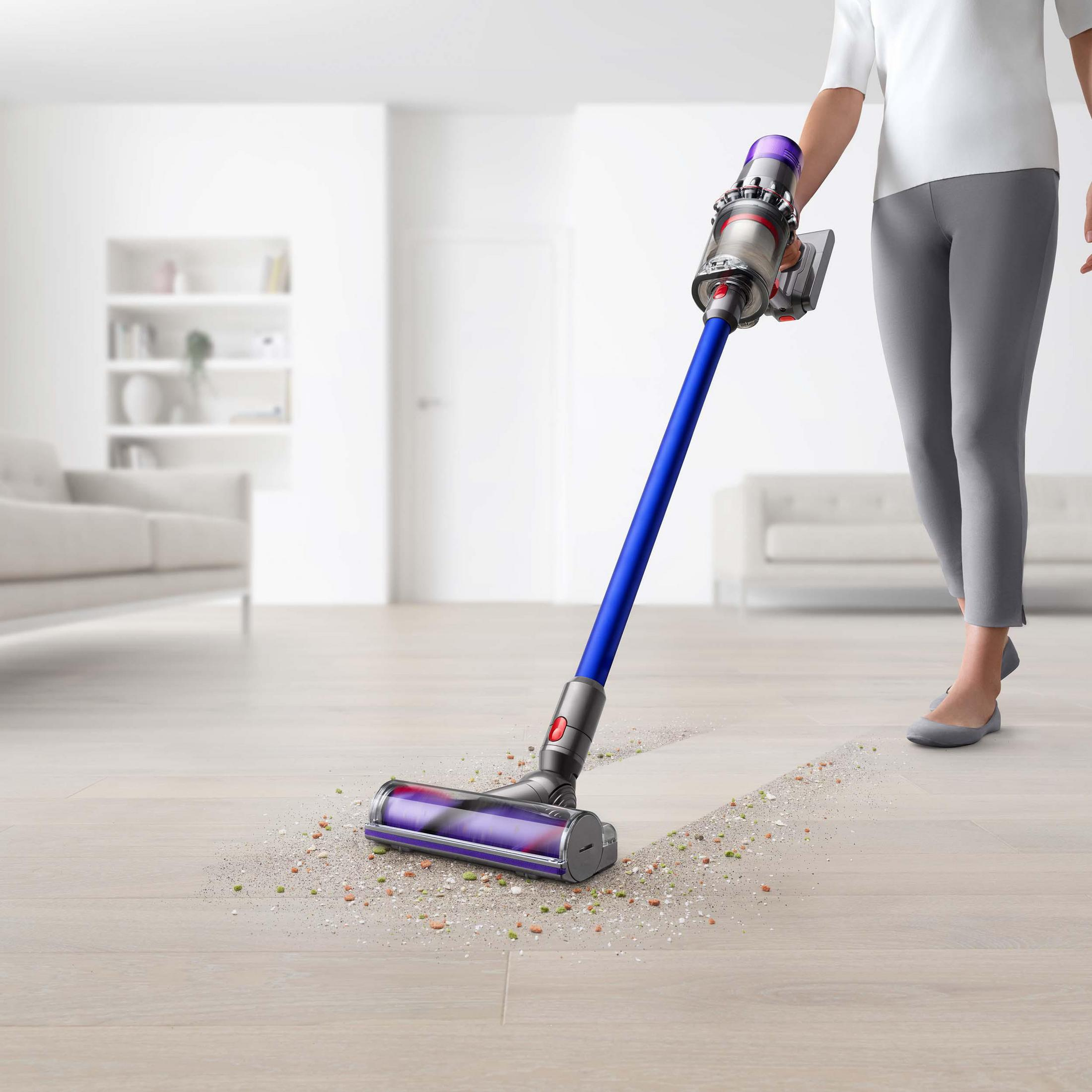 Persona aspirando un piso de madera con una aspiradora azul y morada.