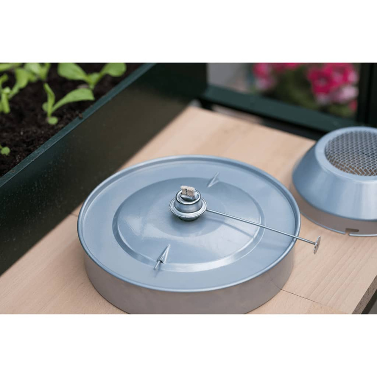 Contenitore metallico con una miccia, usato per il giardinaggio. Un coperchio più piccolo è sullo sfondo.