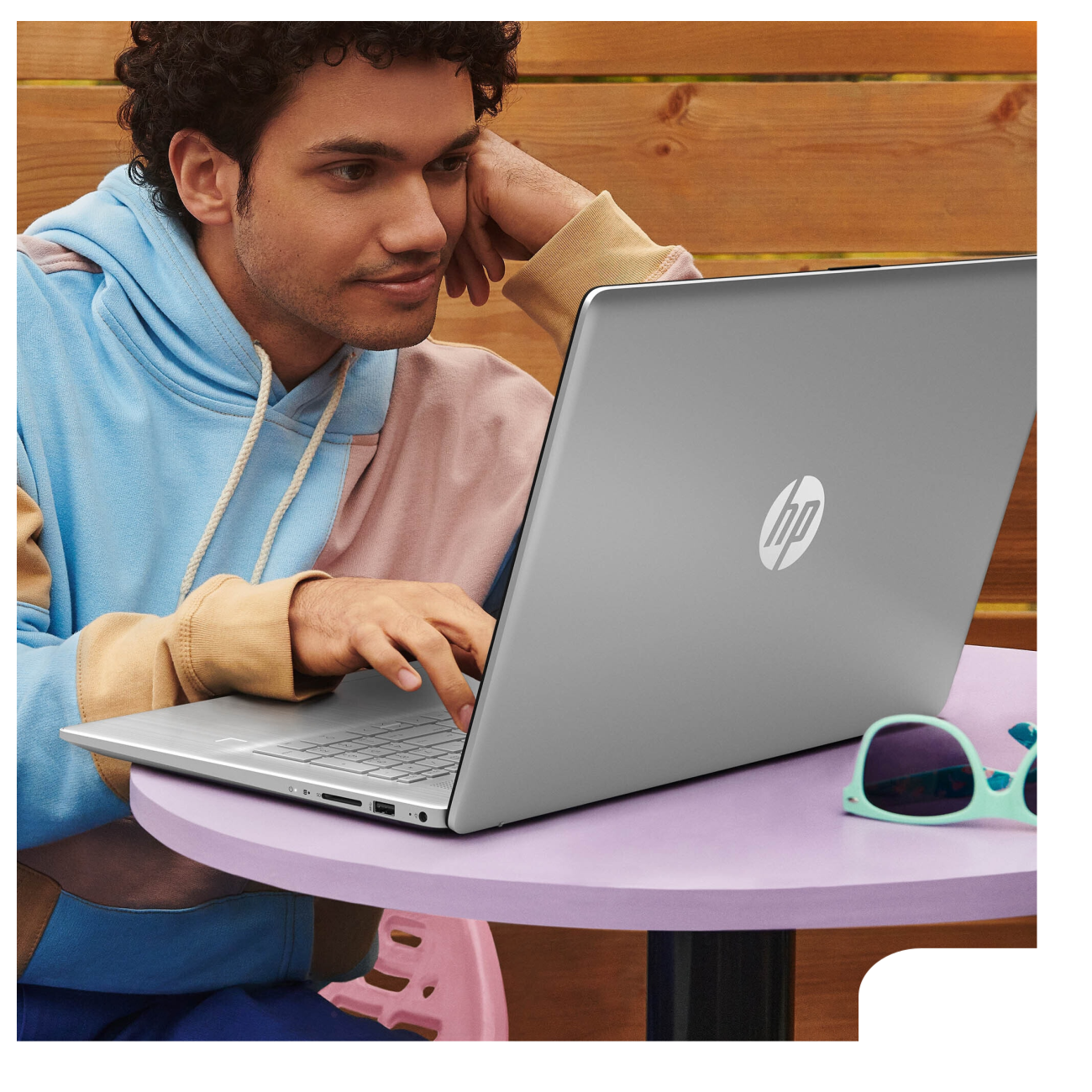 Mann benutzt silbernen Laptop, schaut auf den Bildschirm. Sonnenbrille und Holzhintergrund.