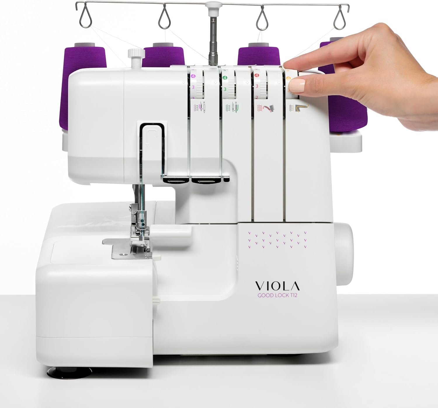 Eine weiße Nähmaschine mit lila Garnspulen. Eine Hand stellt einen Drehknopf ein.