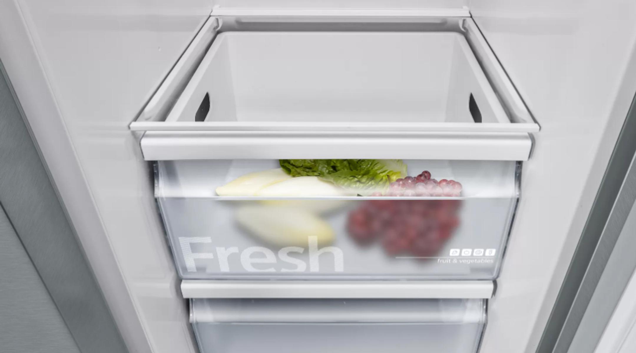 Ein Kühlschrank mit einer durchsichtigen Schublade mit frischen Produkten: Salat, Endivien und Trauben.