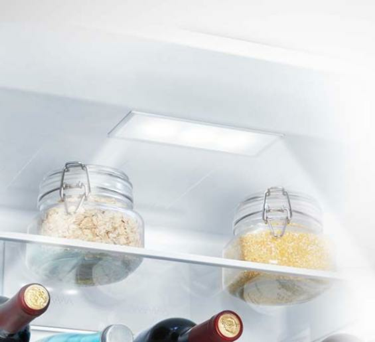 Dentro de un refrigerador con frascos de vidrio llenos de avena y granos. Luz brillante.