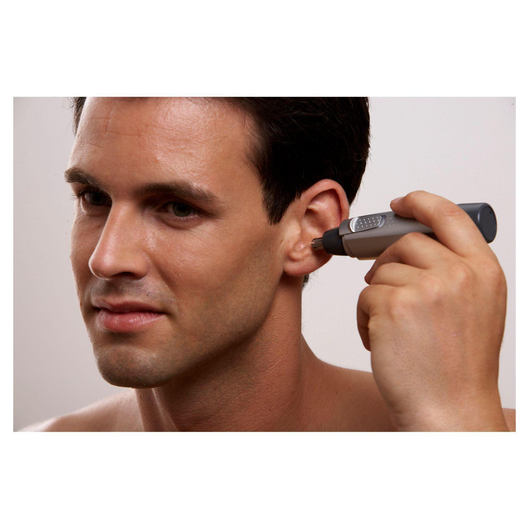 Ein Mann rasiert sich das Ohr mit einem kleinen grauen Trimmer. Er ist ohne Hemd, mit dunklen Haaren und heller Haut.
