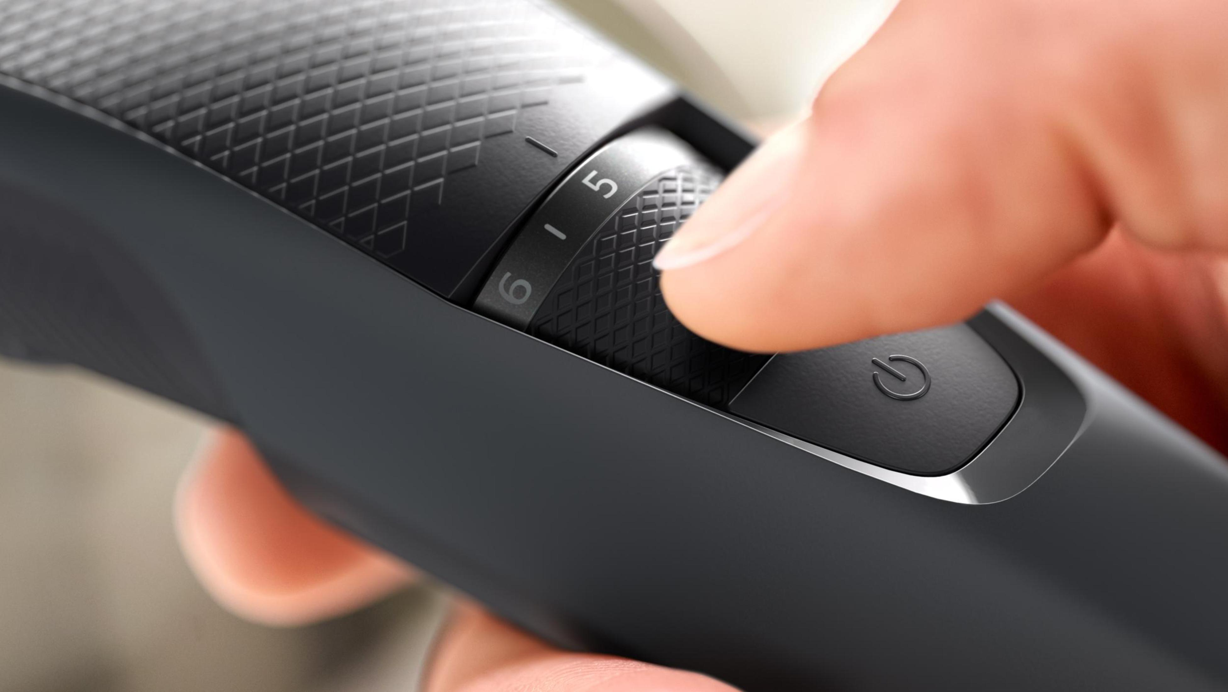 Zbliżenie ciemnoszarej maszynki do strzyżenia włosów z palcem obracającym pokrętło długości.