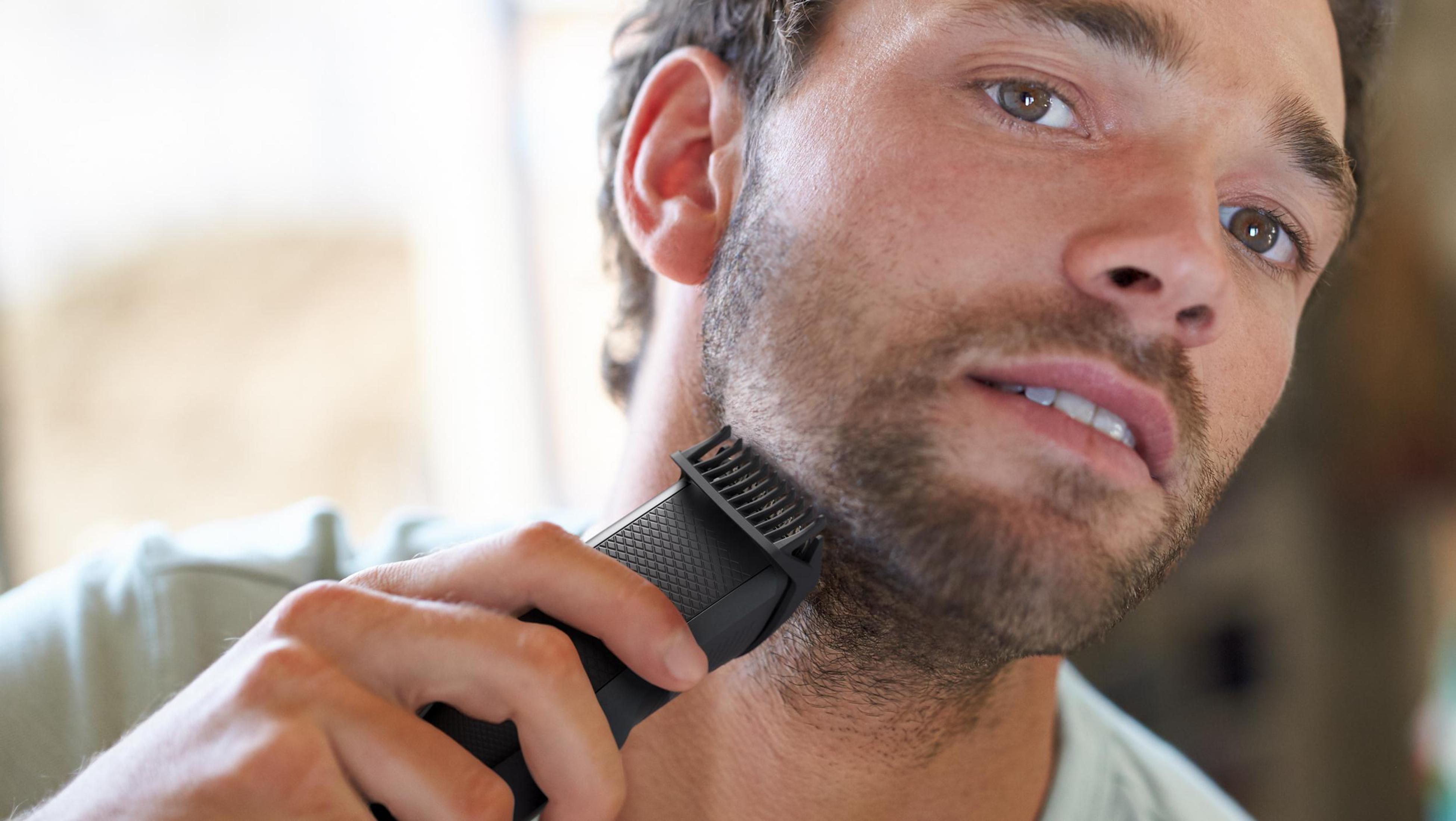 Mężczyzna goli brodę czarną trymerem. Mężczyzna patrzy na trymer.