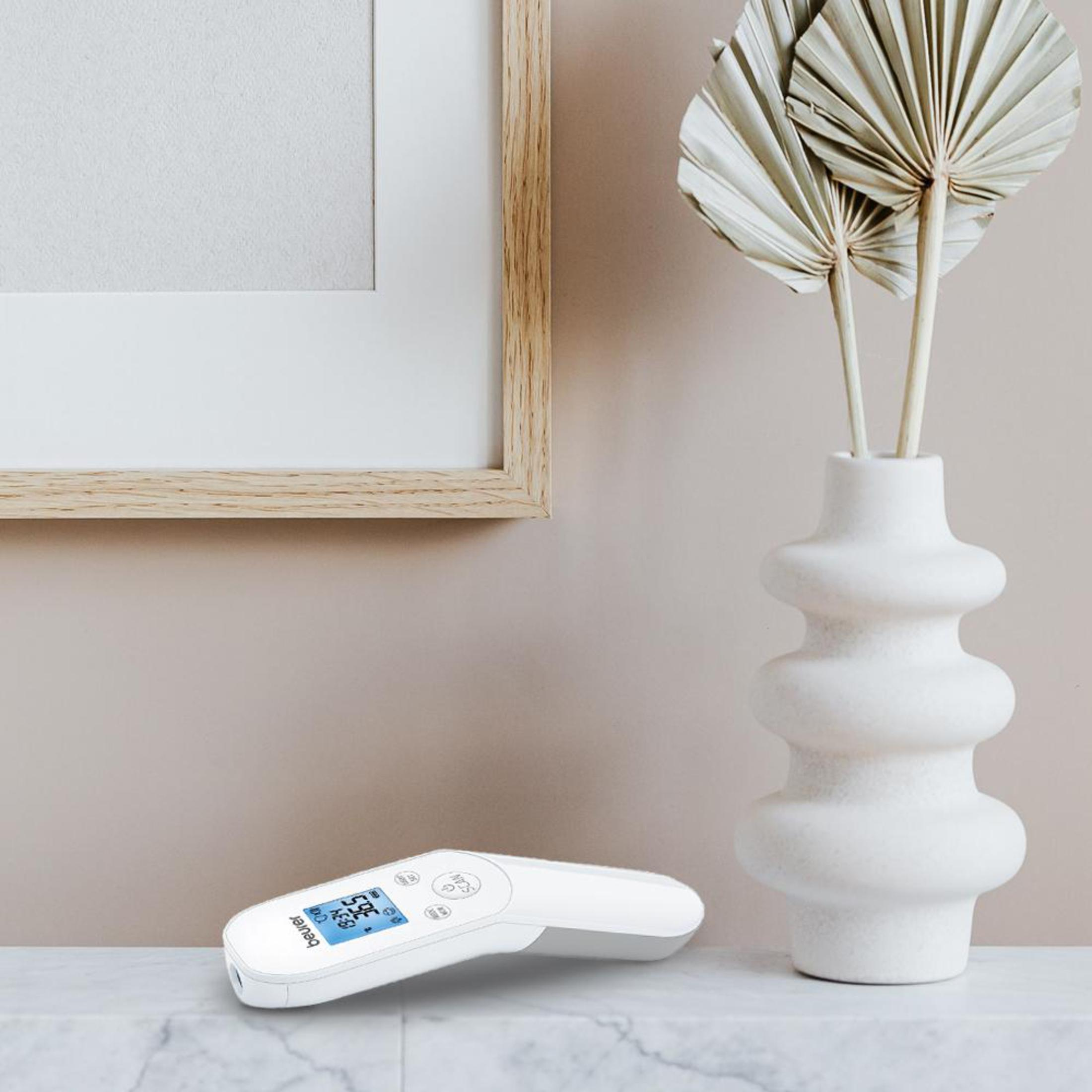A thermometer on a table next to a vase with dried flowers and a picture frame.