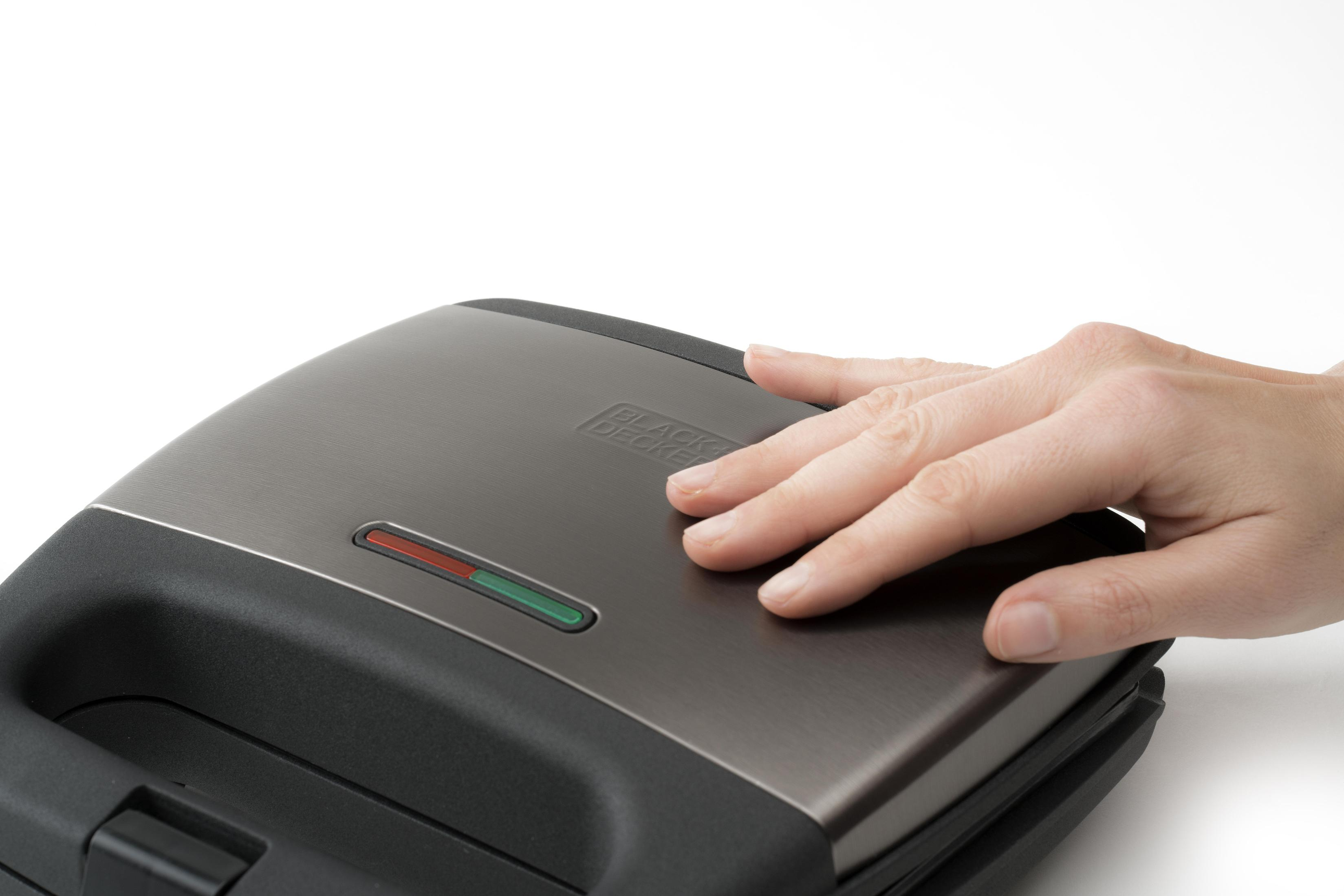 Dłoń dotykająca opiekacza do kanapek; czerwony i zielony wskaźnik.