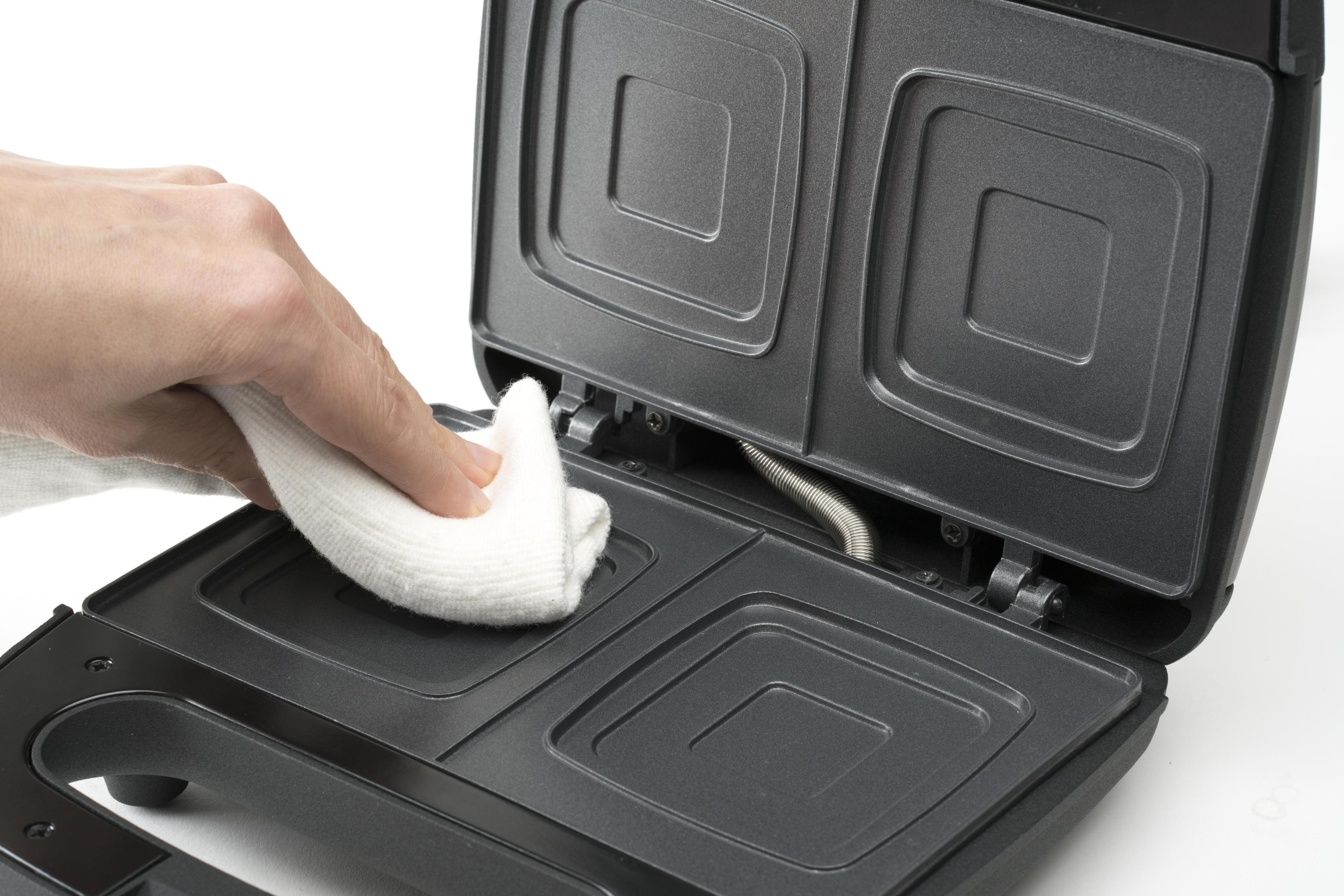 Osoba czyszcząca opiekacz do kanapek białą szmatką, skupiając się na wnętrzu urządzenia.