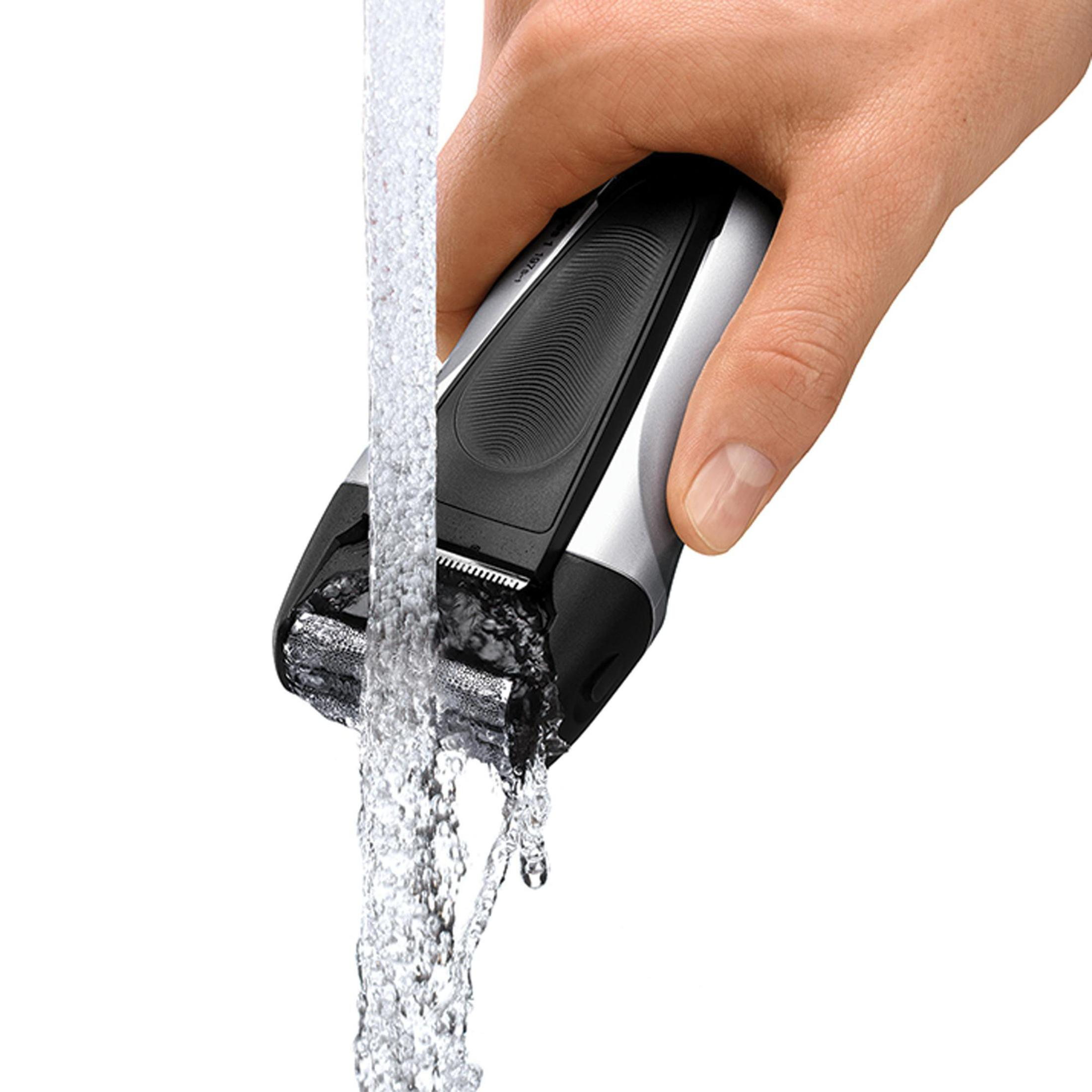 Hand hält schwarzen/silbernen Elektrorasierer unter fließendem Wasser, Rasierkopf nass.