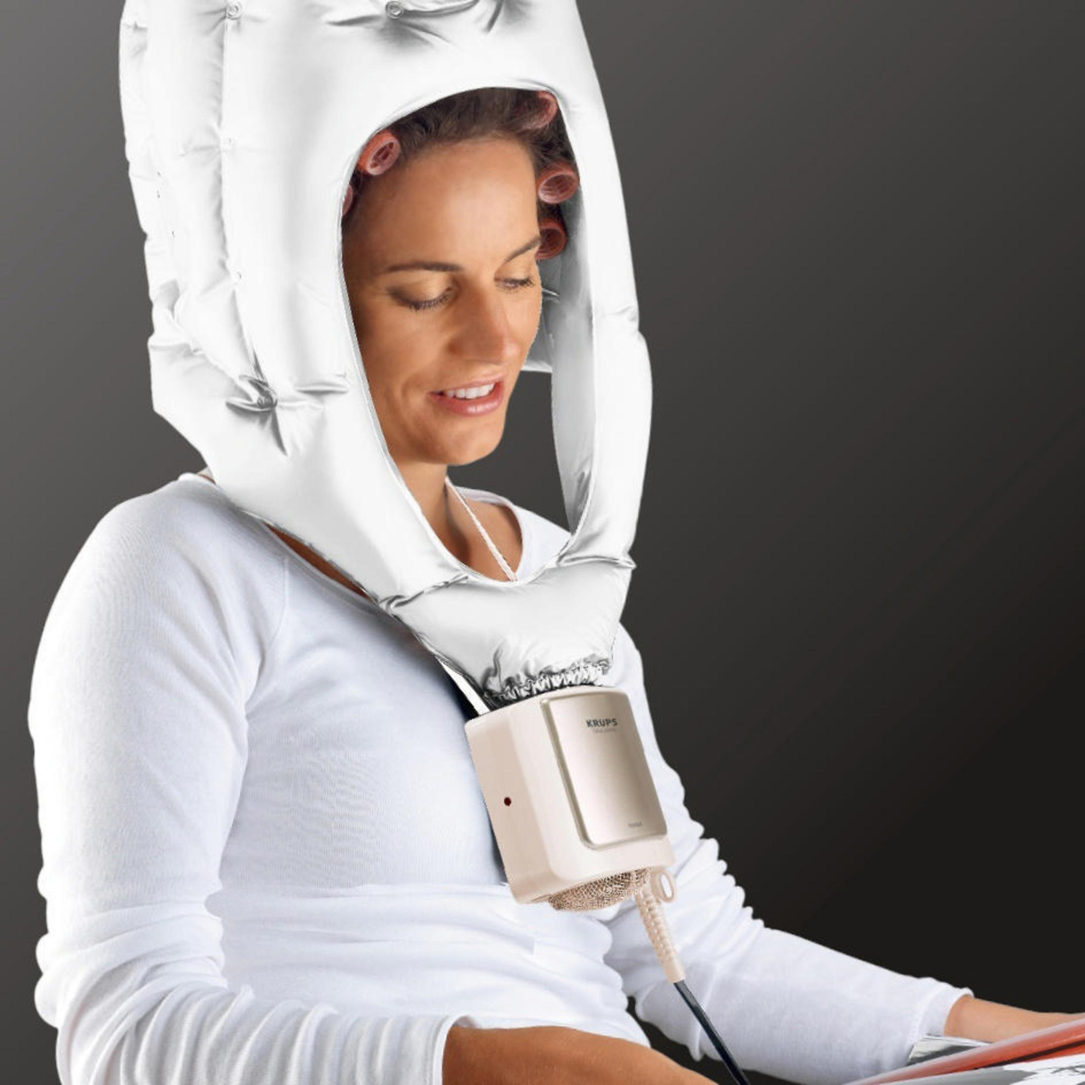 Kobieta z wałkami pod białą suszarką do włosów w kształcie kaptura, z dołączoną beżową suszarką.