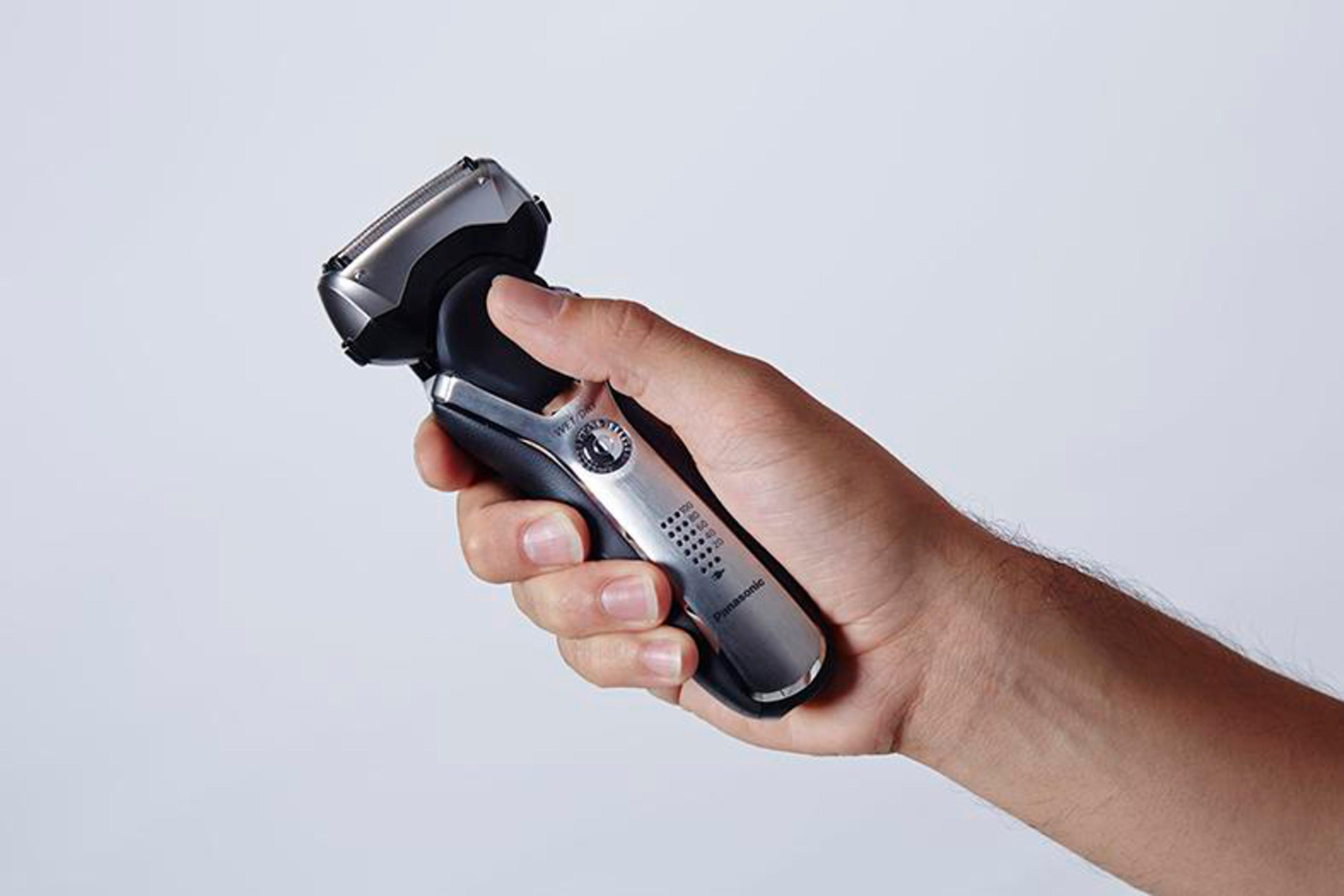 Dłoń trzymająca srebrną golarkę elektryczną. Dłoń jest na białym tle.