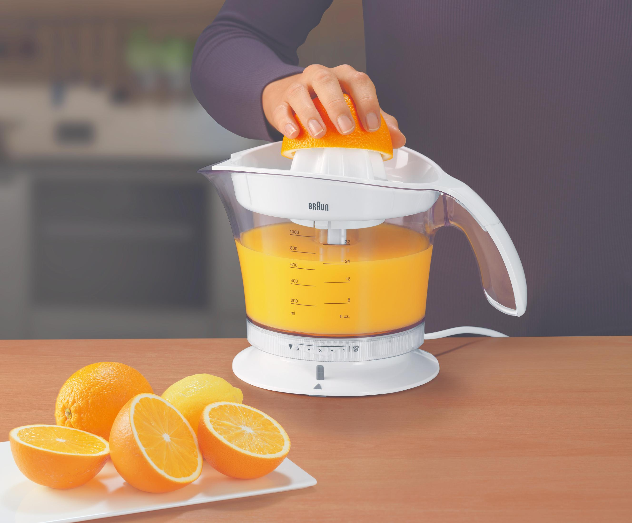 Person drückt eine Orangenhälfte mit einem weißen Entsafter, der Orangensaft enthält. Orangen und Zitrone auf dem Tisch.