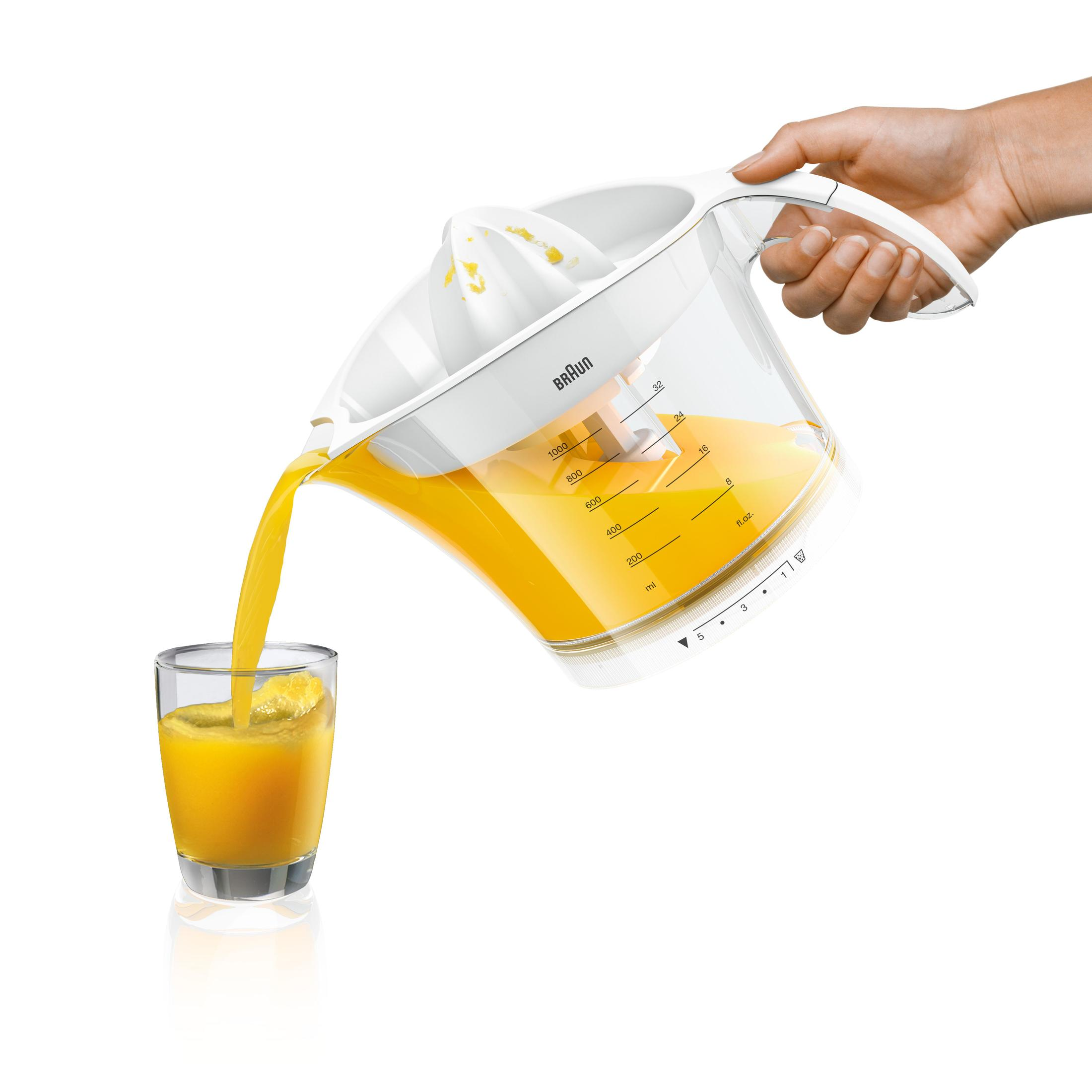 Eine Hand gießt Orangensaft aus einem weißen Entsafter in ein Glas.