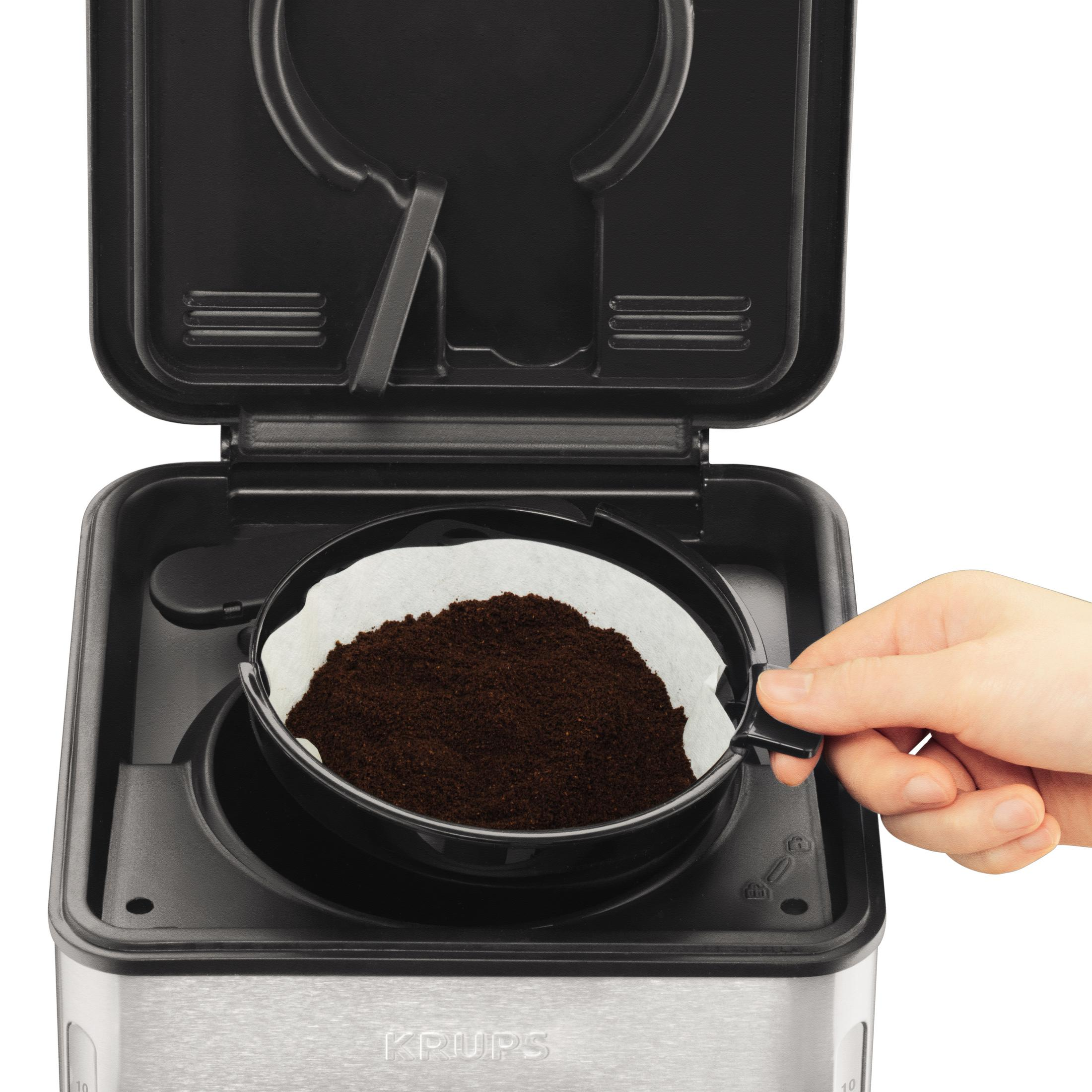 Eine Hand legt einen Papierfilter mit Kaffeepulver in eine Kaffeemaschine. Der Deckel ist offen.