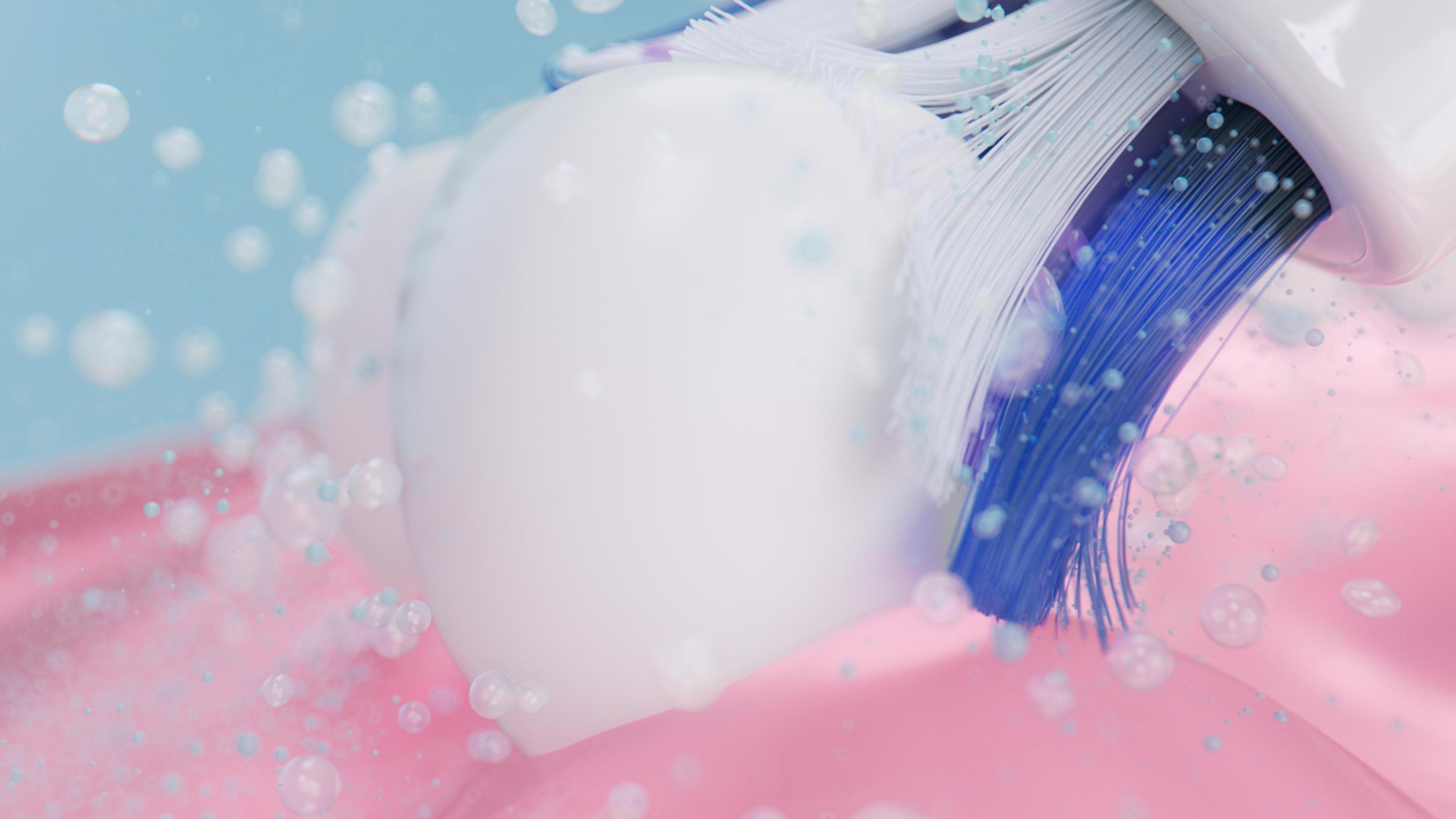 Primo piano di spazzolino con setole blu che pulisce i denti. Dentifricio bianco e gengive rosa visibili.