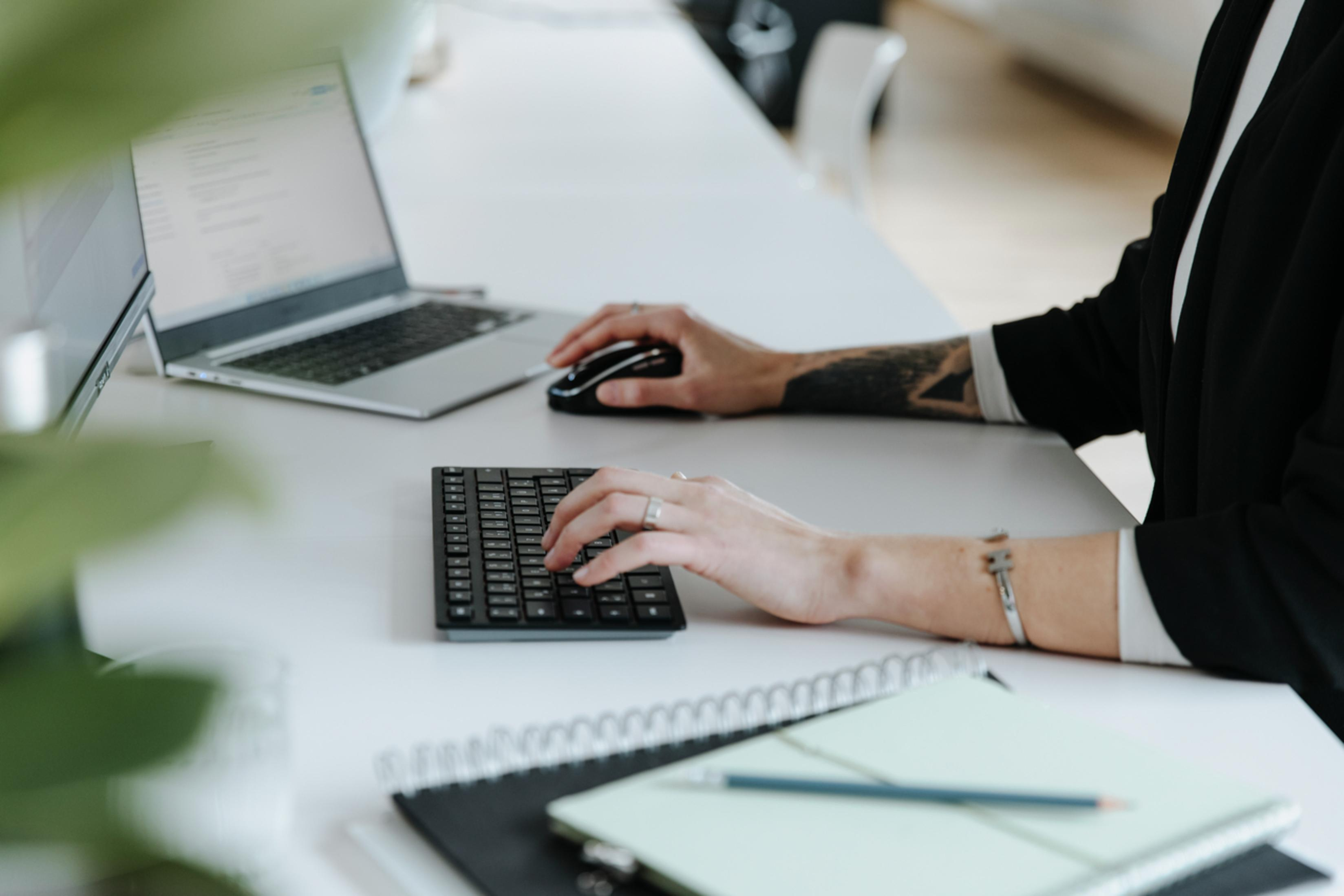Osoba pracuje na laptopie, używając myszy i małej klawiatury.