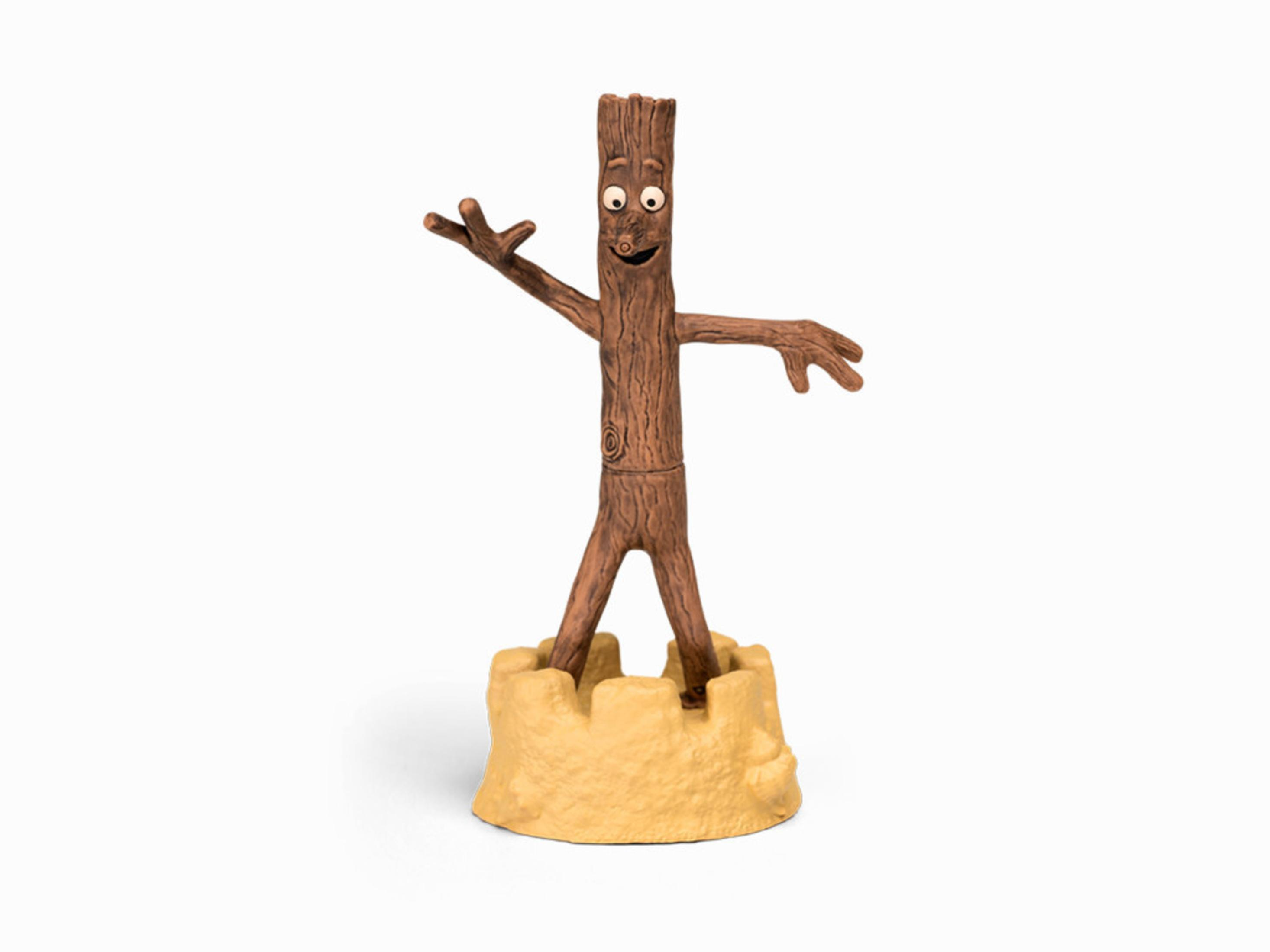 Eine braune Holzstabfigur auf einem beigen Sandburgsockel vor weißem Hintergrund.