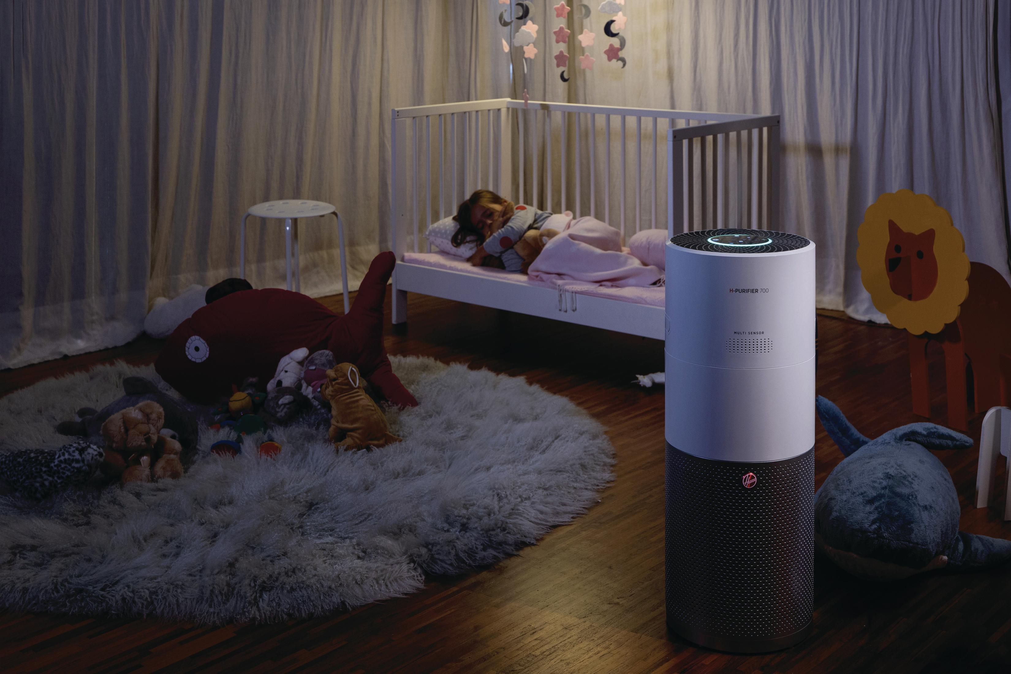 Un bambino dorme in un letto. Un purificatore d'aria è accanto al letto. Giocattoli e un tappeto sono sul pavimento.