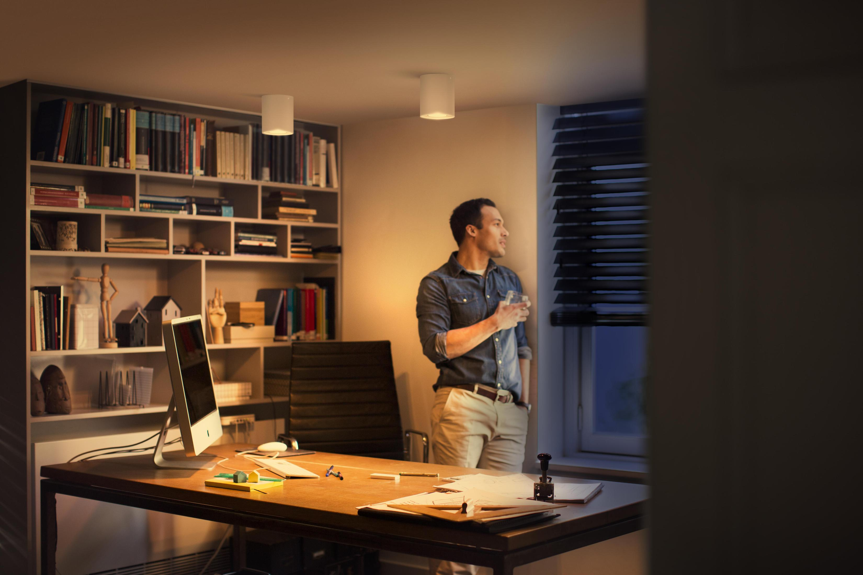 Un homme dans un bureau regardant par la fenêtre tenant un verre d'eau.