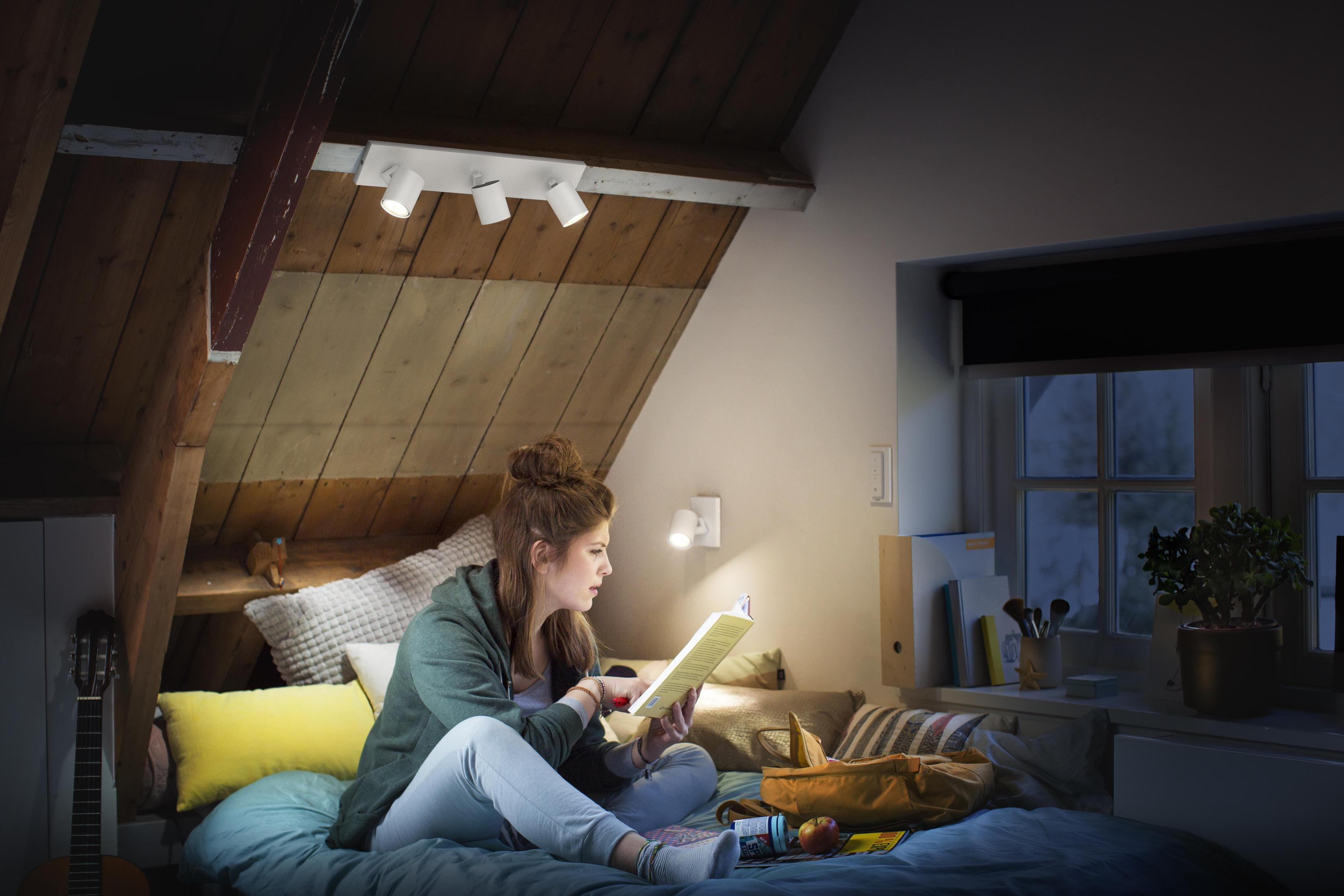 Mujer leyendo un libro bajo luces cálidas en una habitación con techo de madera.