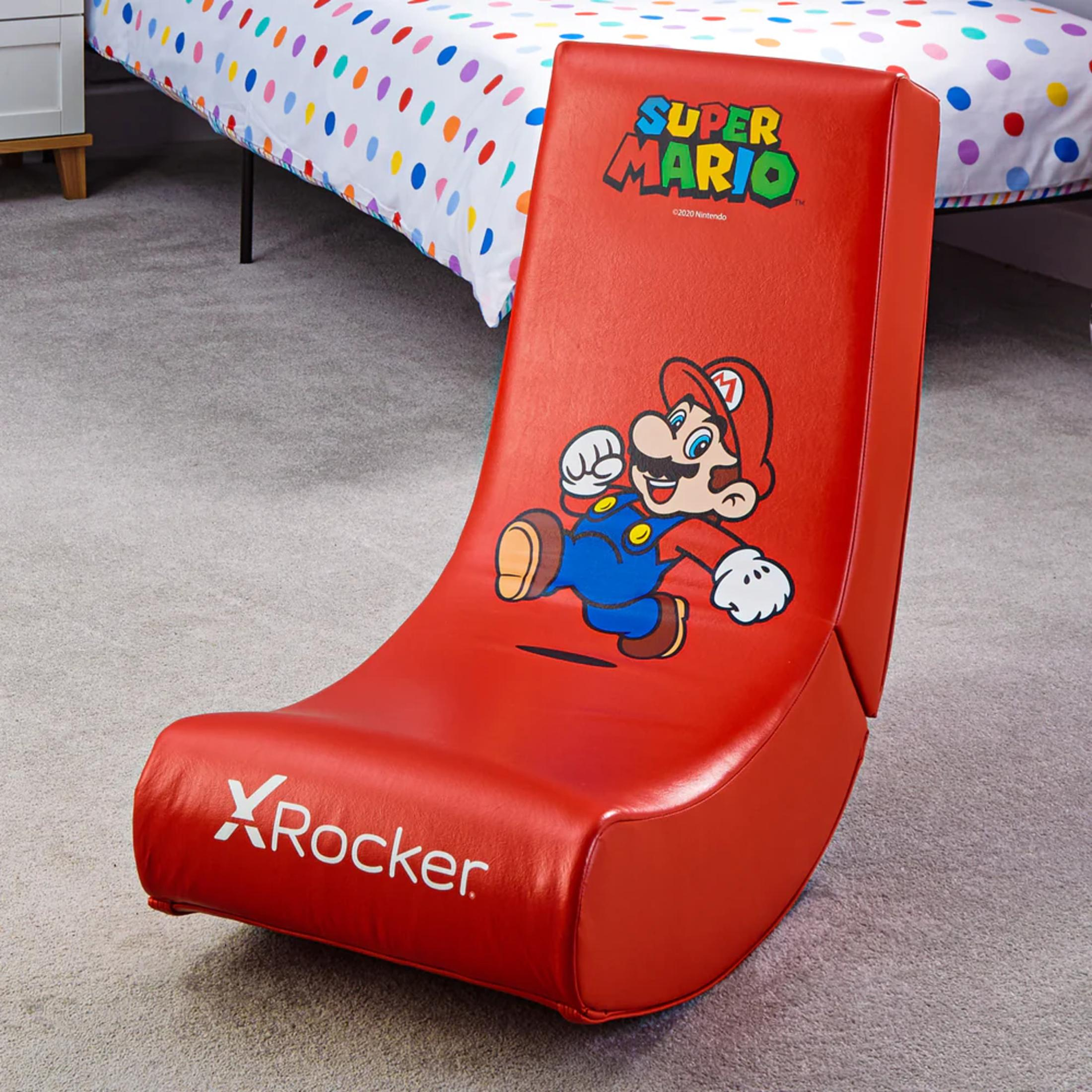 Ein roter Super Mario Schaukelstuhl mit Mario-Grafik. Er steht in einem Raum mit Bett und gemustertem Laken.