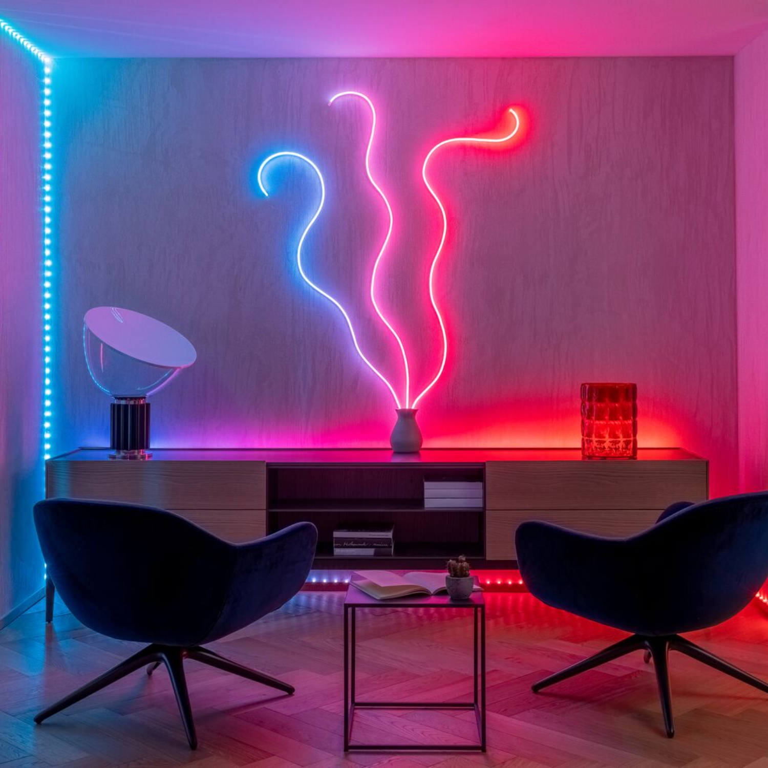 Pokój z neonami. Dwa niebieskie krzesła. Stół z książką i kaktusem. Czerwone światła.