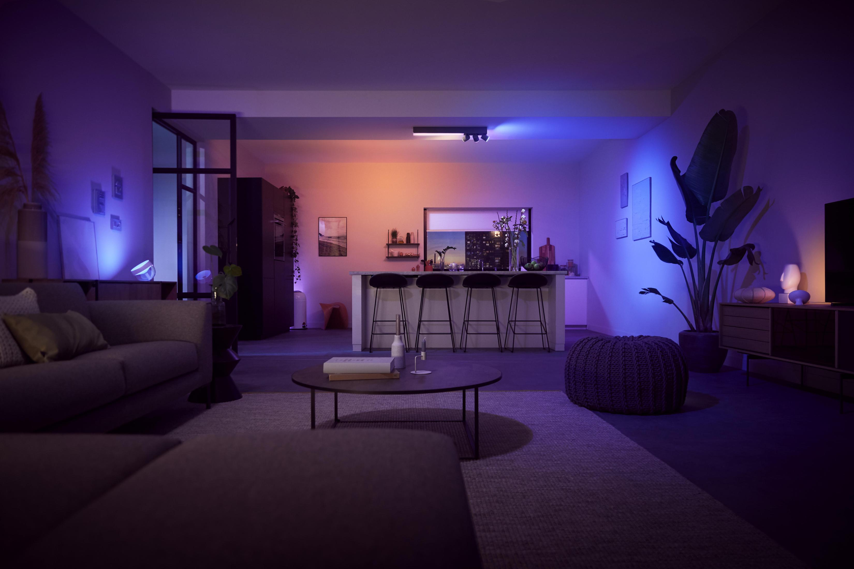 Un moderno soggiorno con illuminazione intelligente. Divano, tavolino, piante e una cucina sullo sfondo.