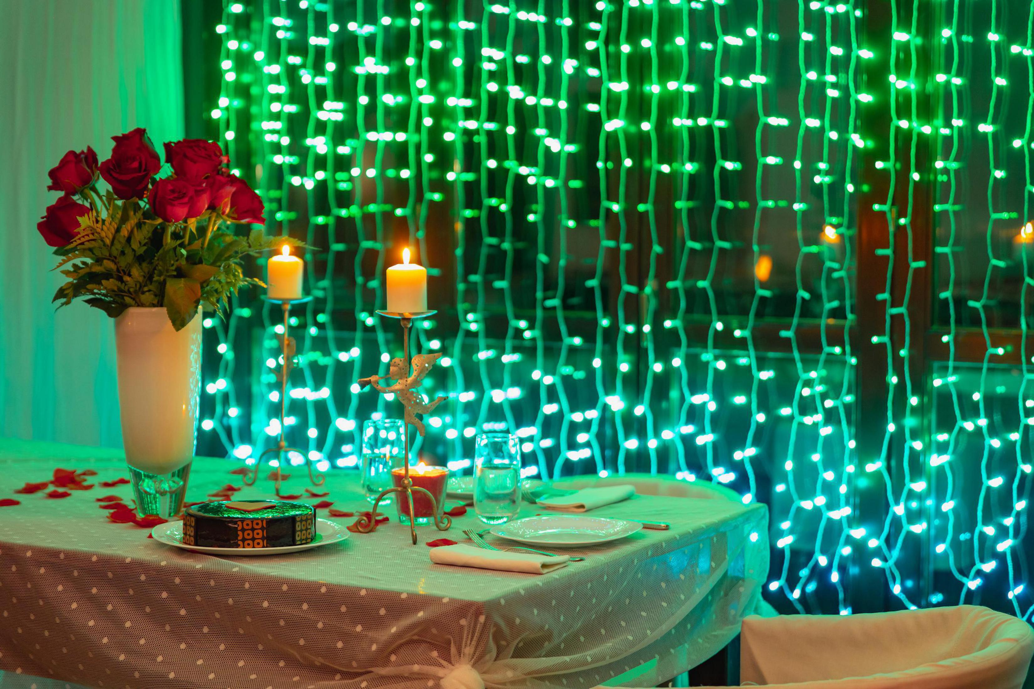 Romantyczna kolacja z różami, świecami i ciastem na stole z lampkami choinkowymi.