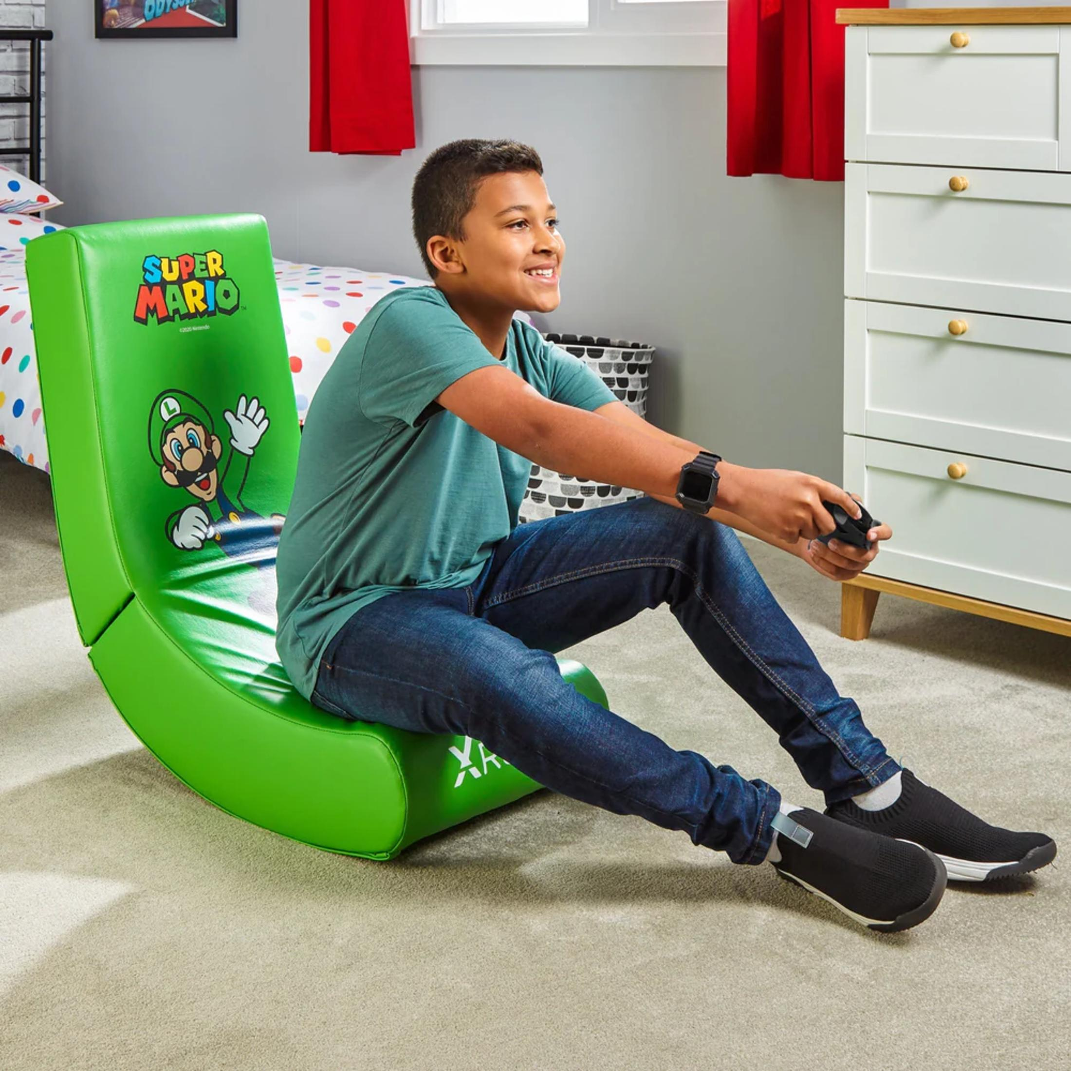 Jongen zit in een groene Super Mario stoel, speelt een spel, glimlacht.