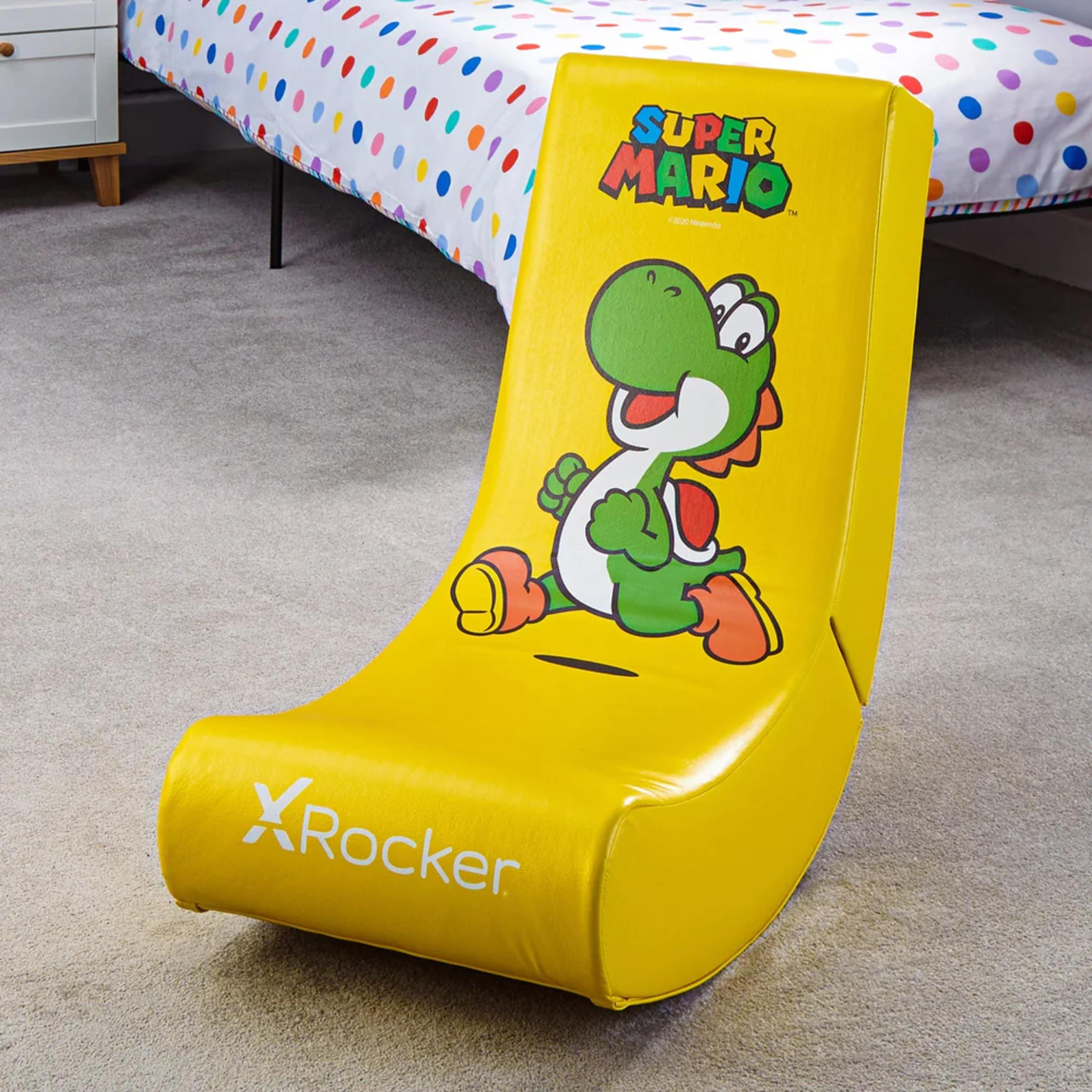 Een gele Super Mario Yoshi schommelstoel staat op een tapijt, bed met een kleurrijk gestippeld laken op de achtergrond.