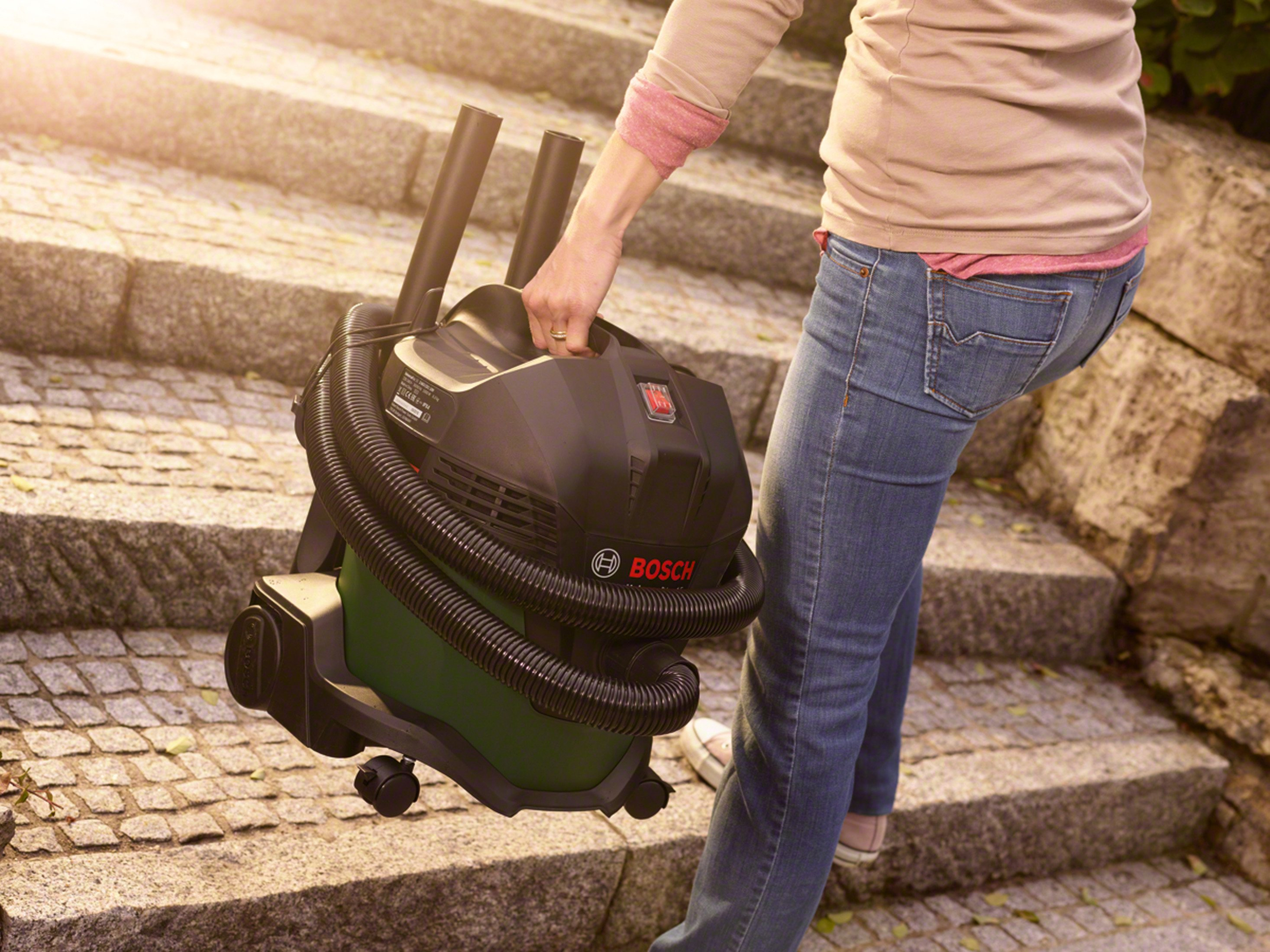 Una persona che trasporta un aspirapolvere Bosch nero e verde sulle scale.