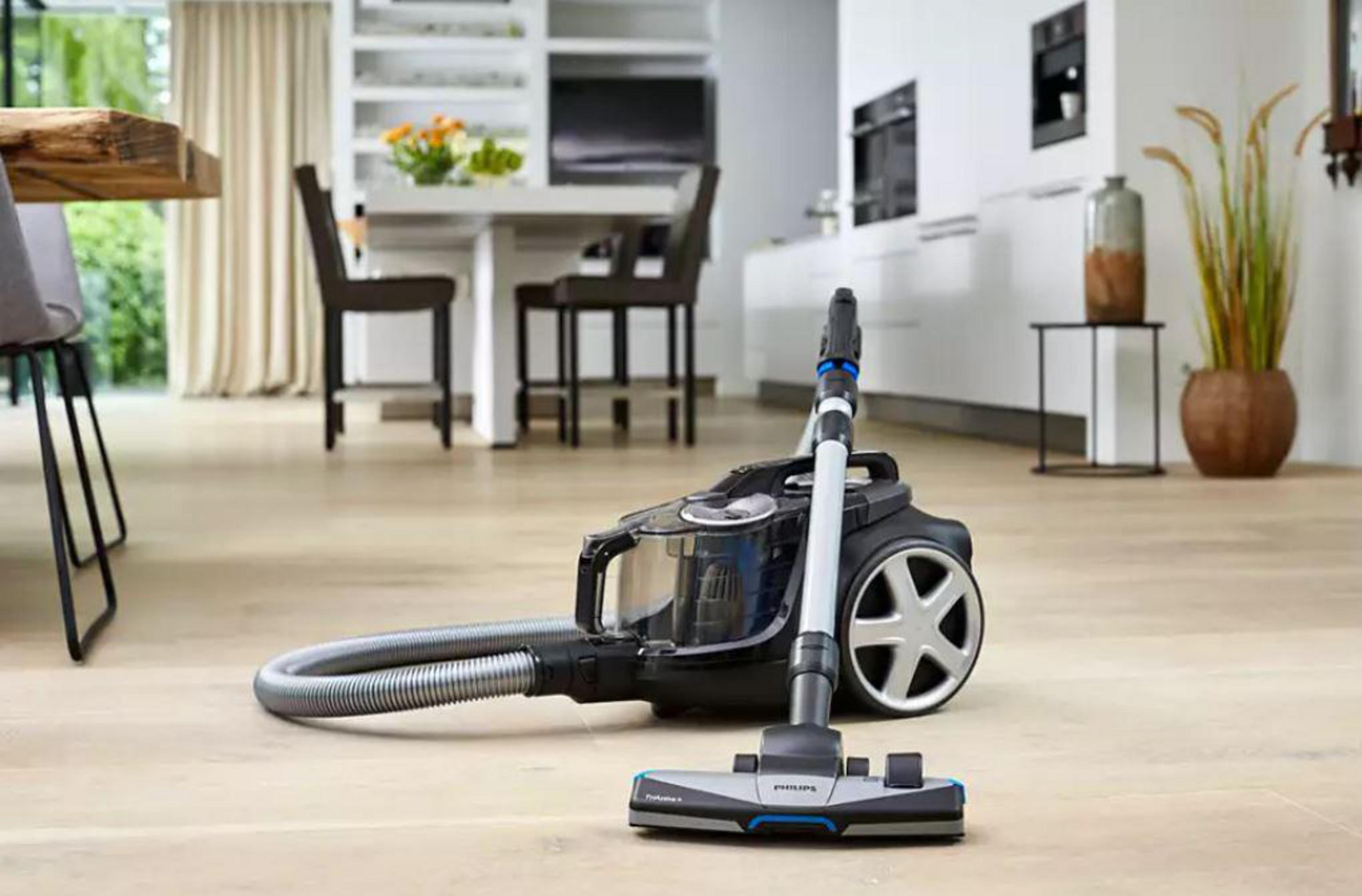 Aspiradora en un piso de madera. La manguera y la cabeza están en primer plano.