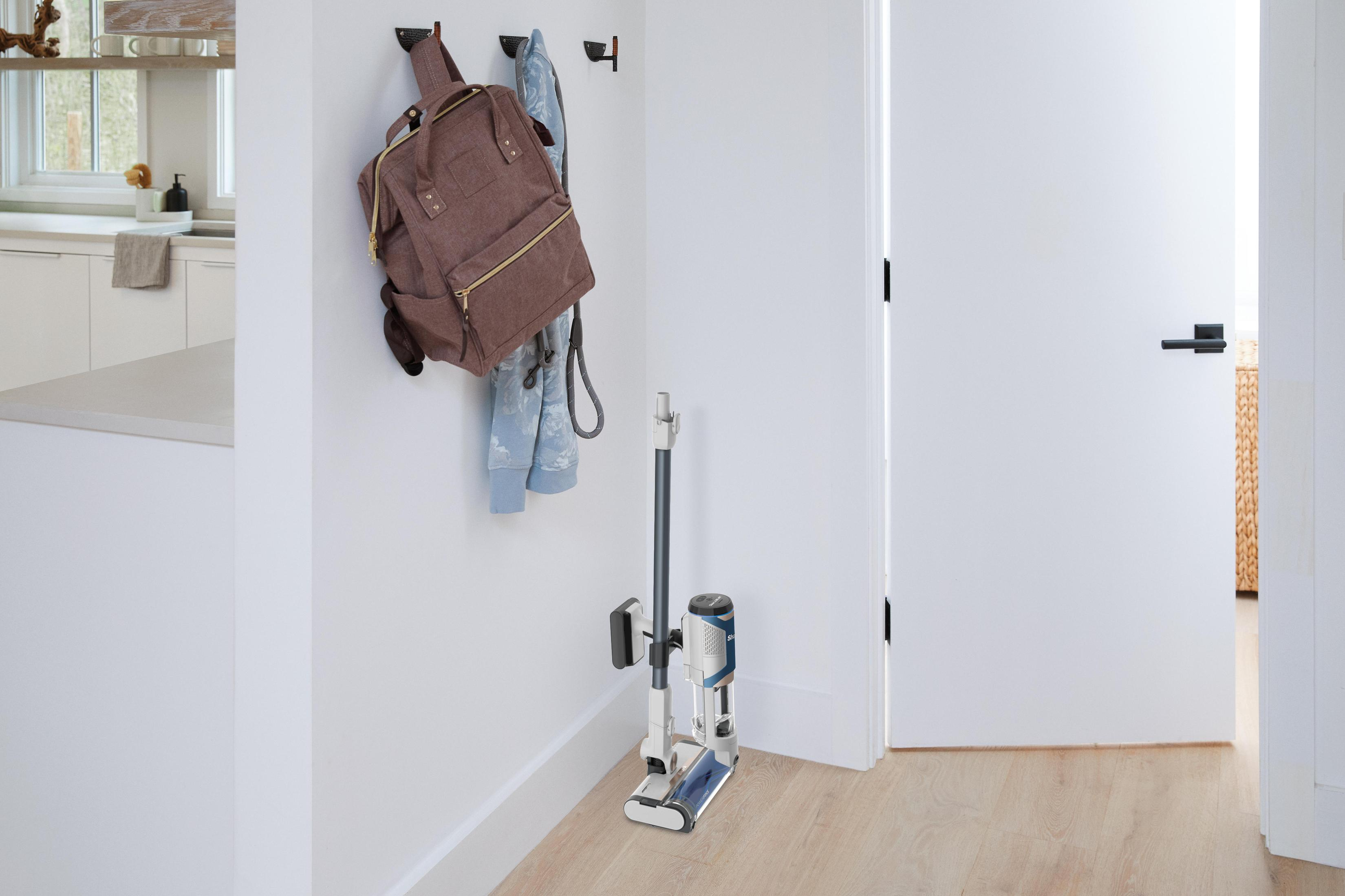 Eingangsbereich mit Rucksack, Jacke und Staubsauger. Weiße Wände und Holzboden.