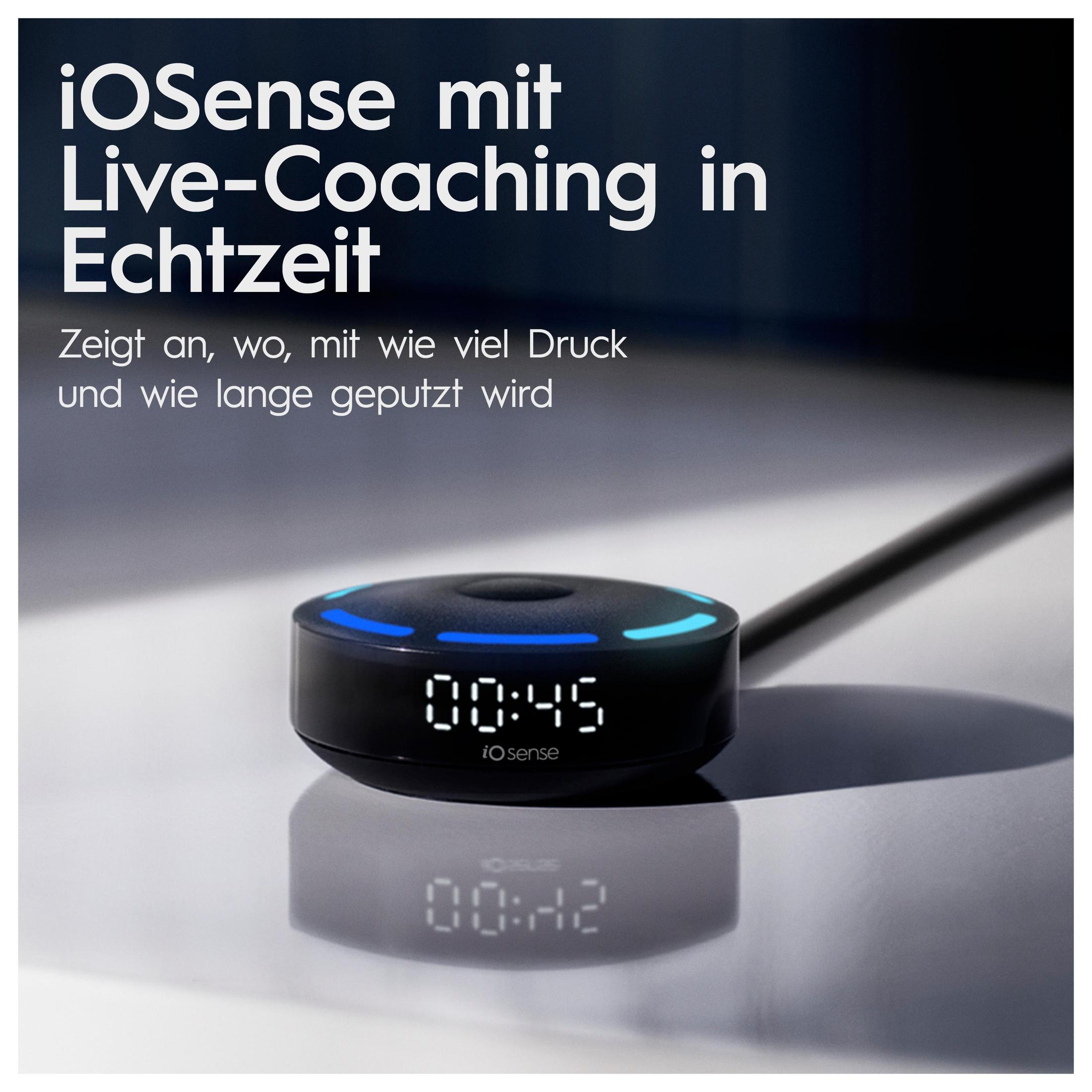 Czarne urządzenie z ekranem pokazującym godzinę. Znajduje się na białej powierzchni z odbiciem.