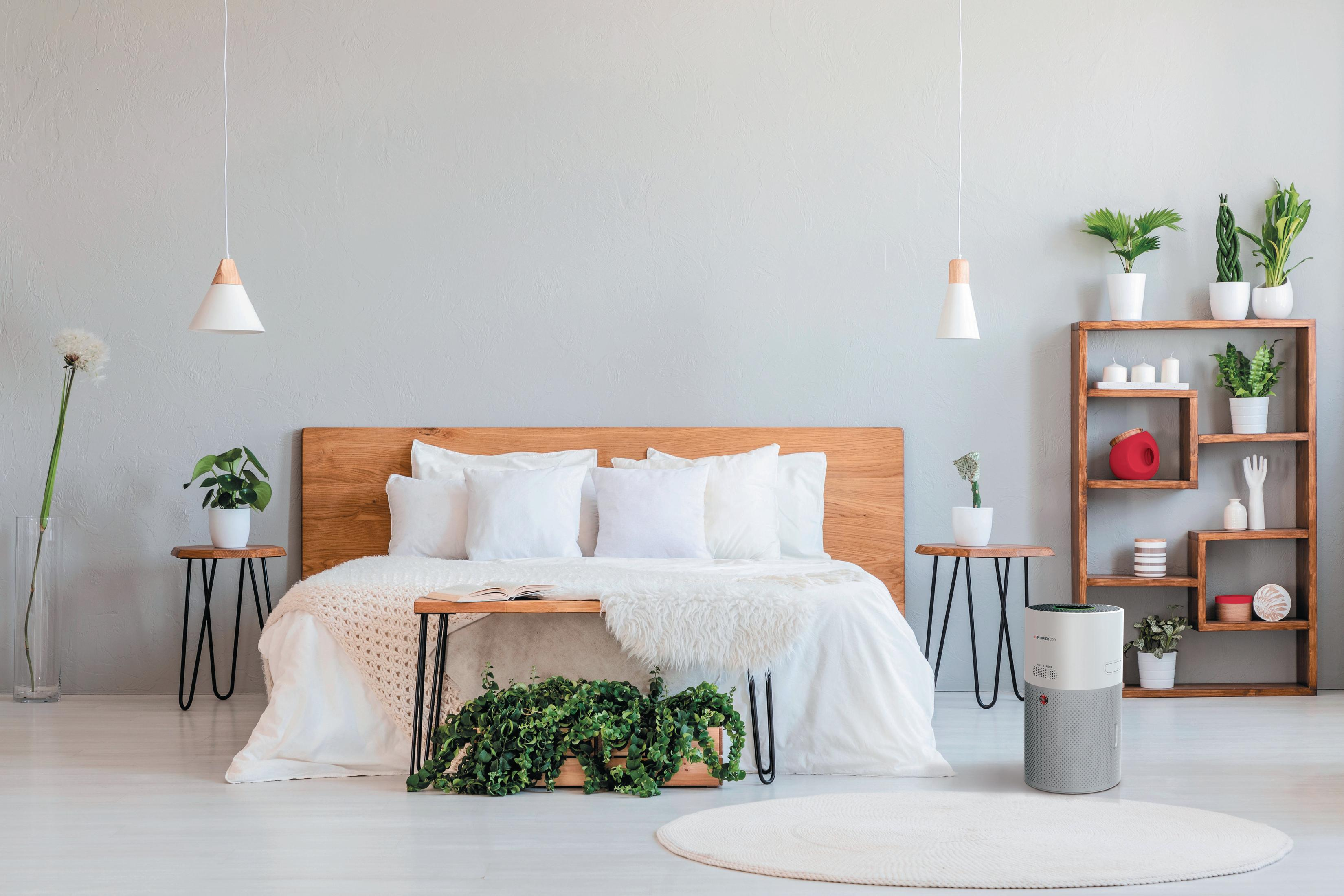 Schlafzimmer mit Bett, Pflanzen und Luftreiniger. Neutrale Farben und natürliches Licht schaffen eine ruhige Atmosphäre.