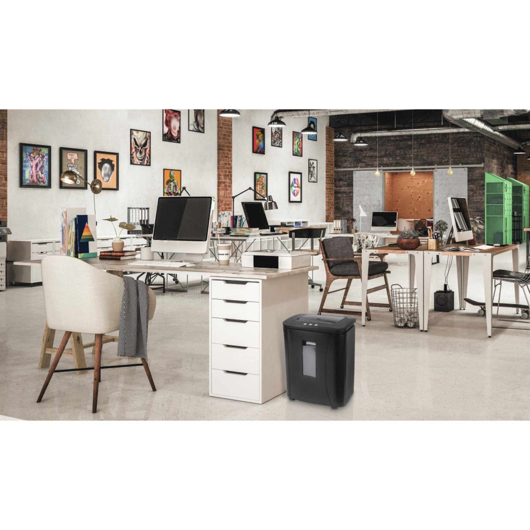 Otoczenie biurowe z biurkami, komputerami, sztuką i czarną niszczarką do papieru.