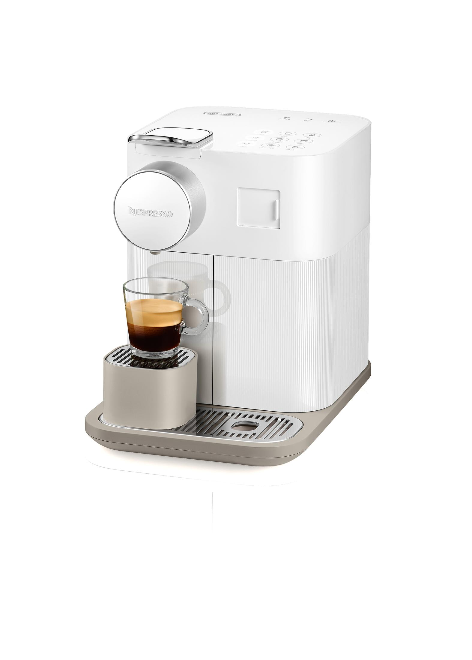 Nespresso-Kaffeemaschine, weiß mit silbernen Akzenten, mit einem Glas Espresso, auf weißer Oberfläche.