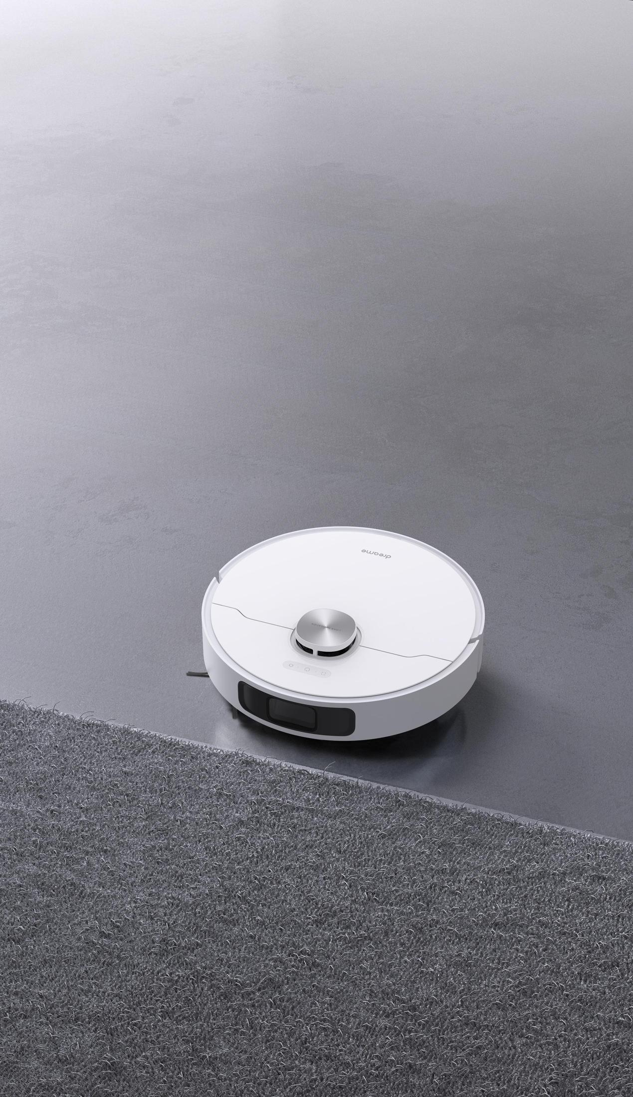 Aspirapolvere robot bianco su un pavimento grigio, vicino a un tappeto. Il robot ha una parte superiore argentata.